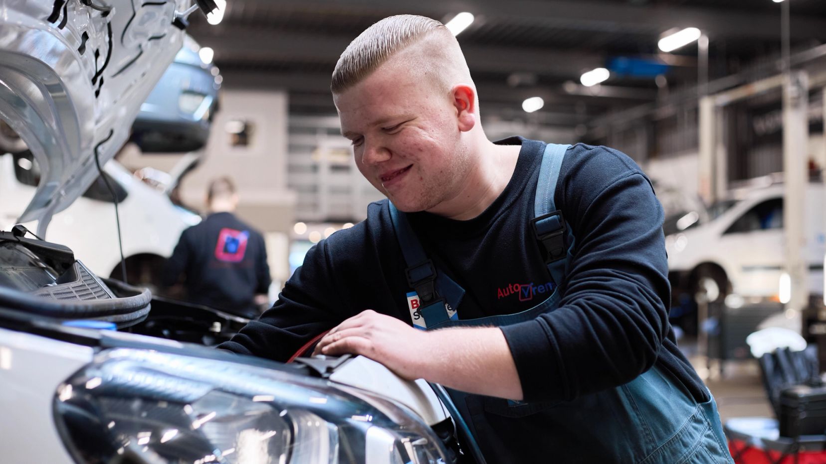 Lachende monteur in overall werkt onder de motorkap van een auto.