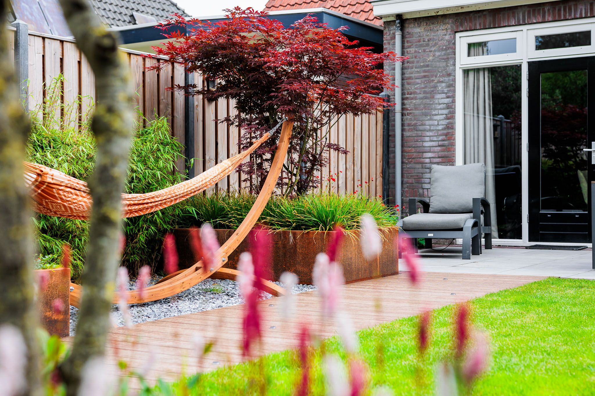 Hangmat onder een rode esdoorn met roze bloemen op de voorgrond.