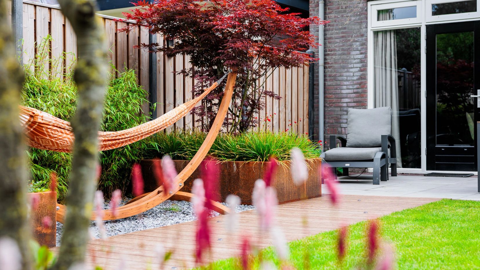 Hangmat onder een rode esdoorn met roze bloemen op de voorgrond.