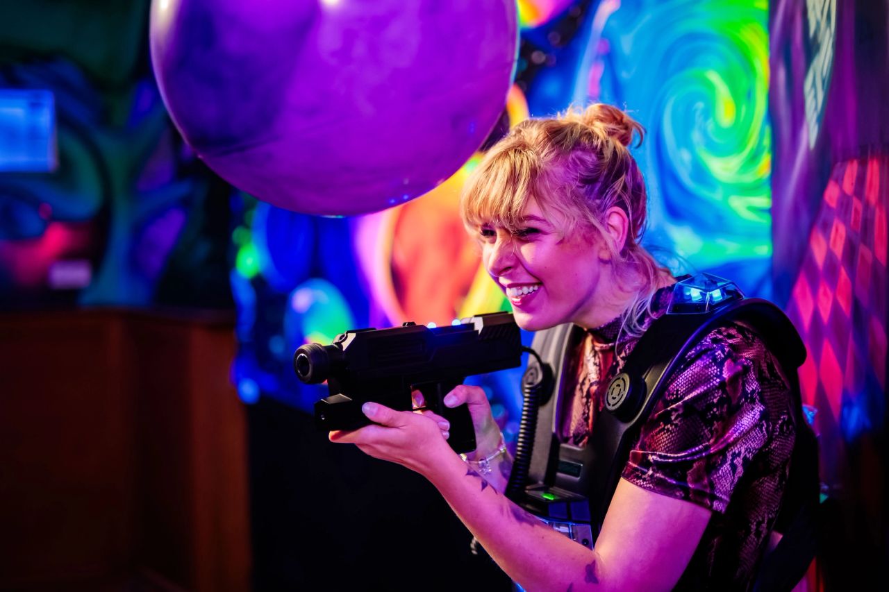 Lachende speelster met lasergamepistool en paarse ballon bij Timestamp Arnhem.