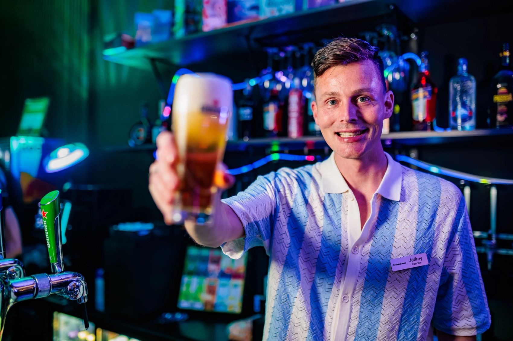 Lachende barman houdt een glas bier omhoog achter de bar bij Timestamp Arnhem, gemaakt door Bold Productions