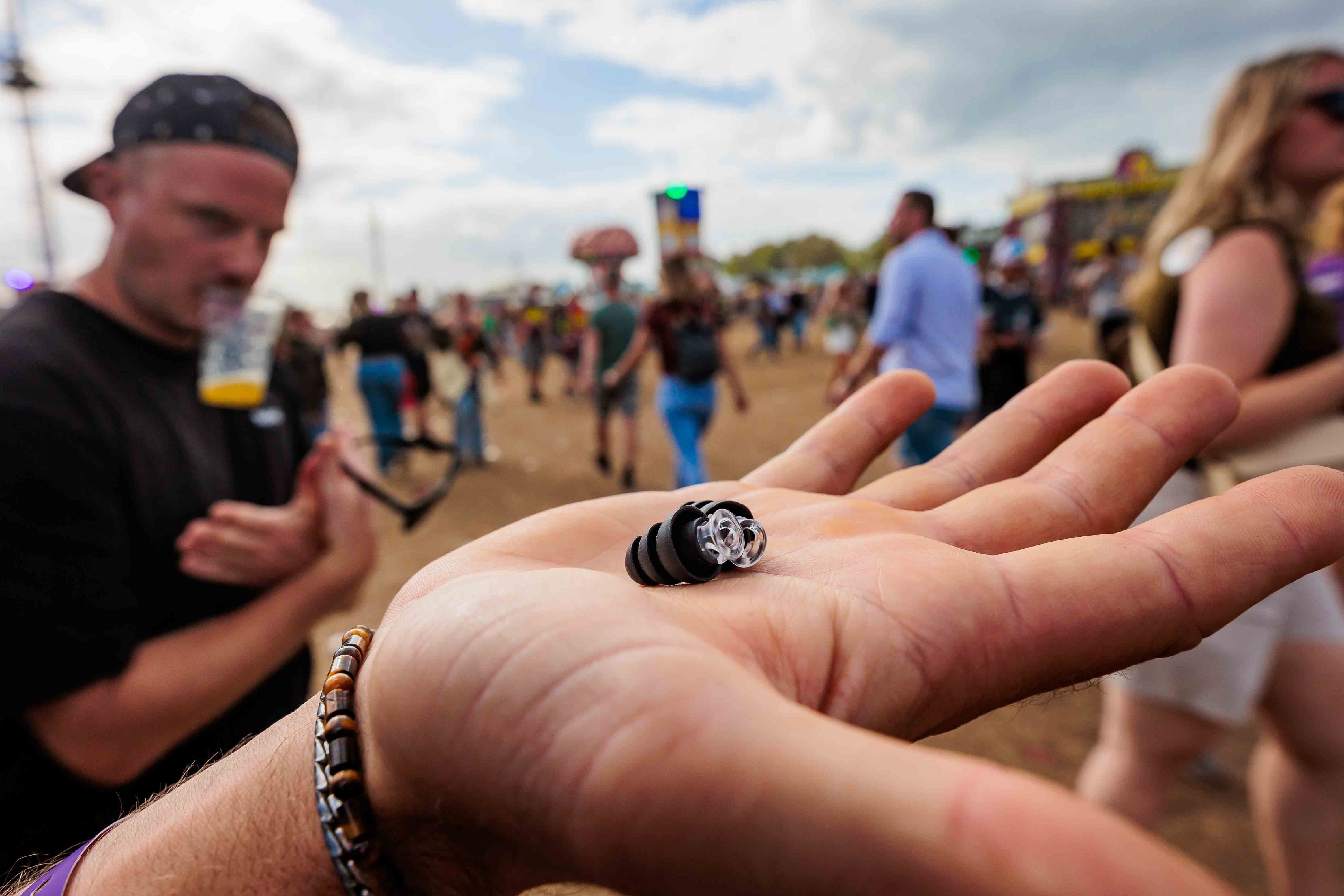 Open hand met een klein oordopje, met festivalgangers onscherp op de achtergrond, gemaakt door Bold Productions