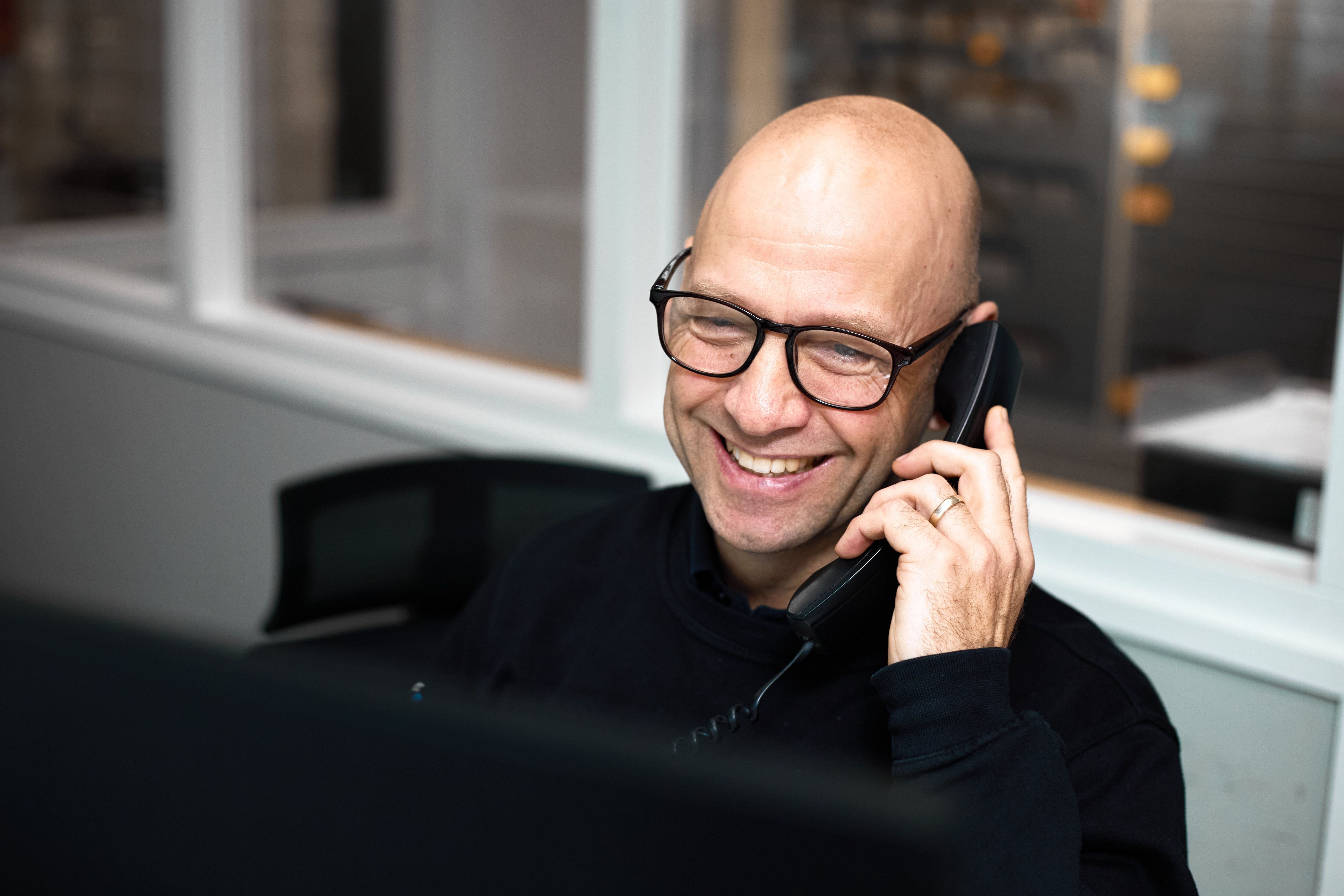 Lachende medewerker belt aan zijn bureau bij Auto Vreman.