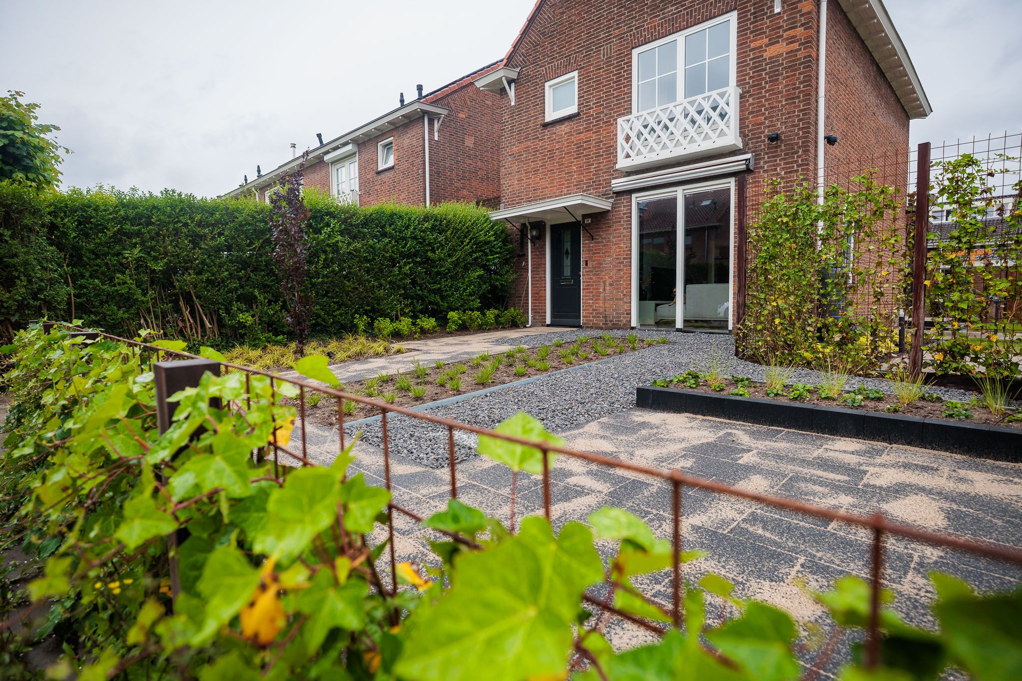 Voortuin met roestkleurige klimframes, haag en klinkers voor een rijwoning.