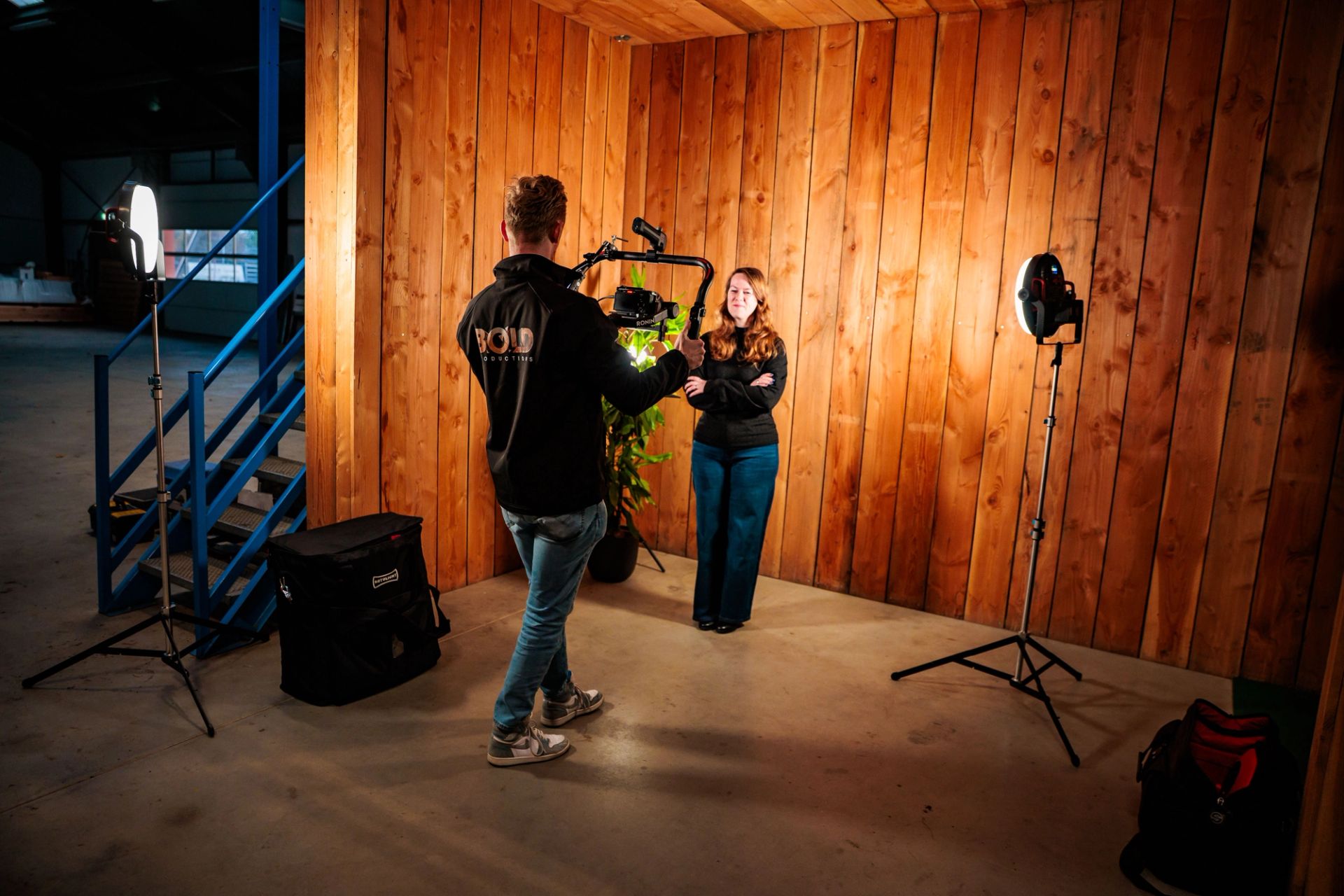 Twee mensen tijdens een opname op een houten set met studiolampen en statieven, gemaakt door Bold Productions