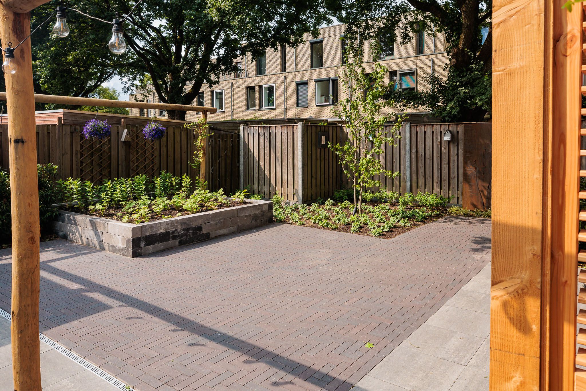 Stadstuin met terras van grijze klinkers, houten pergola en verhoogde border.