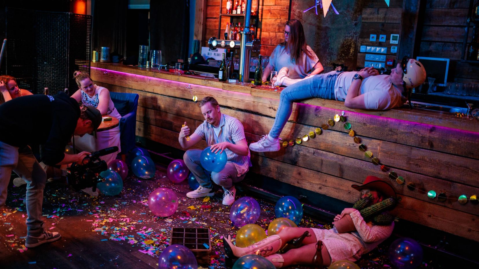 Gasten ontspannen rond een houten bar met slingers en confetti in een rustiek café, gemaakt door Bold Productions