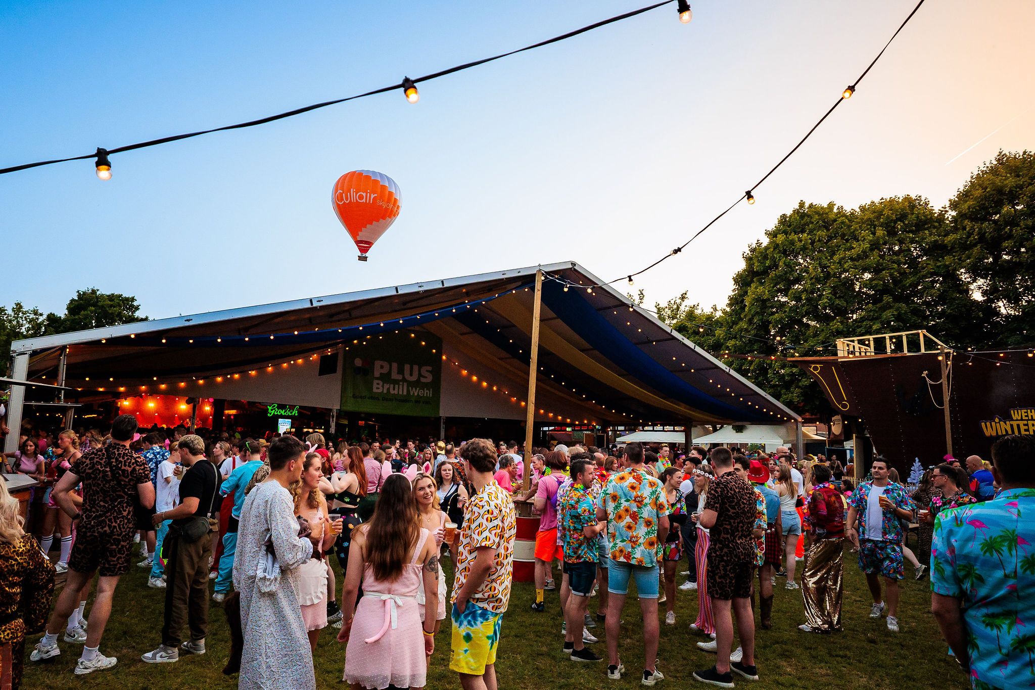 Feesttent met een luchtballon op de achtergrond en bezoekers in de avondzon tijdens het Dorpsfeest in Wehl, gemaakt door Bold Productions