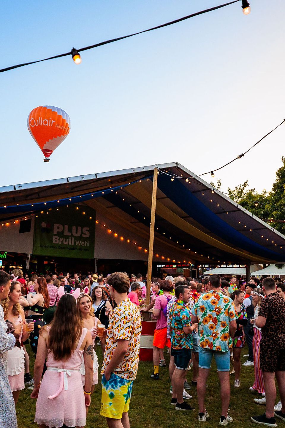 Feesttent met een luchtballon op de achtergrond en bezoekers in de avondzon tijdens het Dorpsfeest in Wehl, gemaakt door Bold Productions
