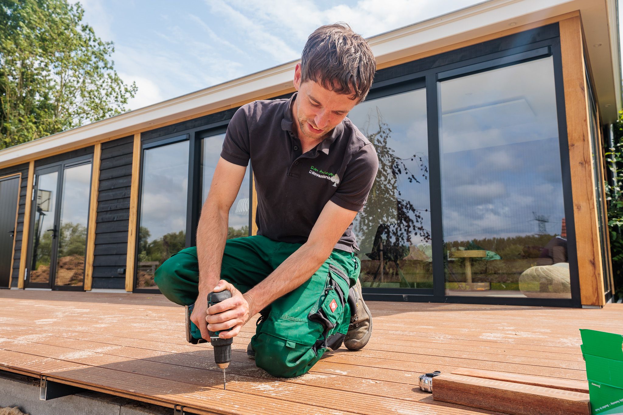 Hovenier legt een houten vlonder aan bij een tuinkamer.