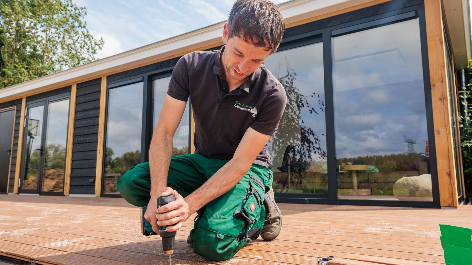 Hovenier legt een houten vlonder aan bij een tuinkamer.