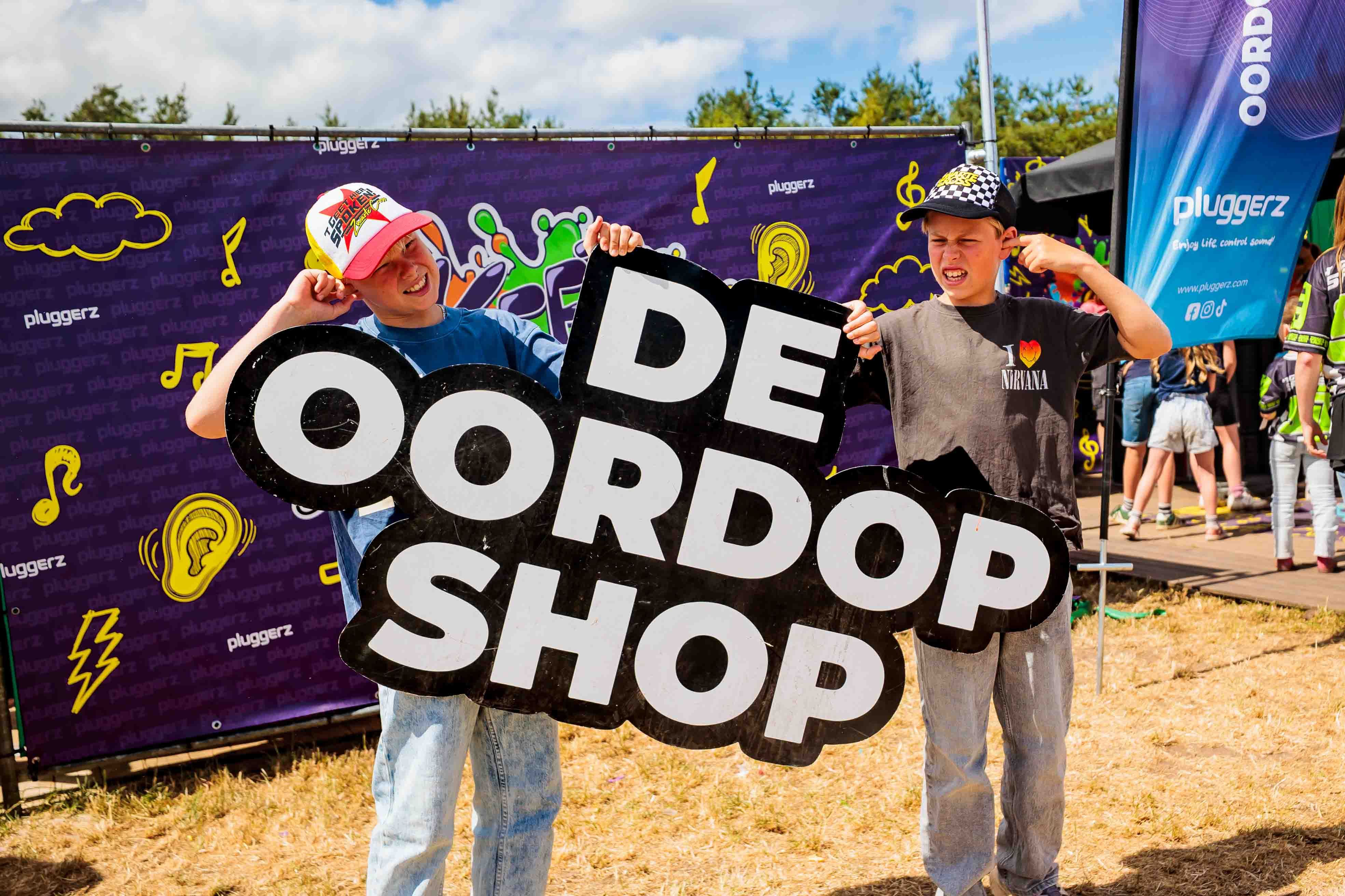 Bord met de tekst De Oordopshop voor een paarse wand met muzieknoten op het festivalterrein, gemaakt door Bold Productions