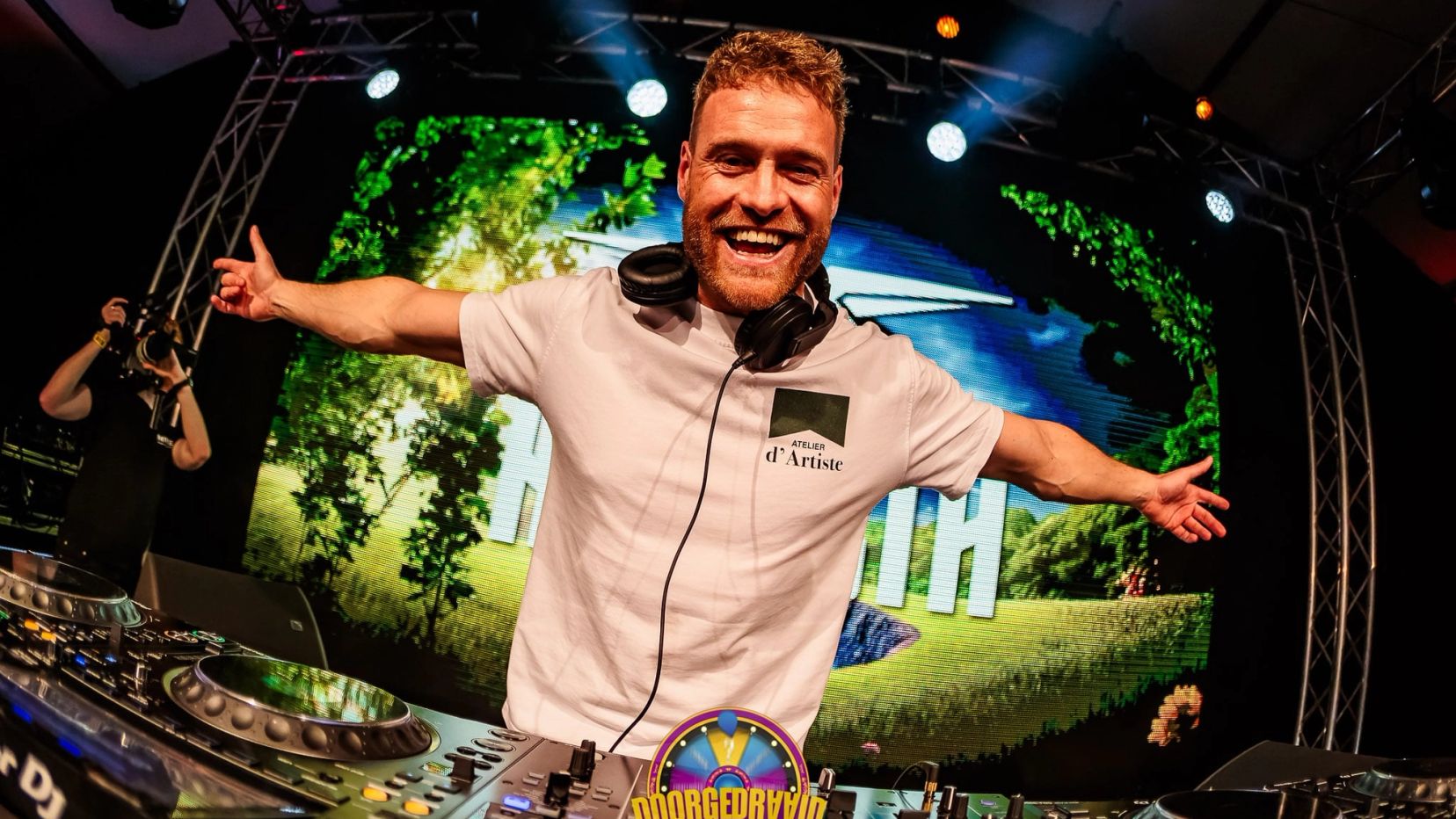 DJ in een wit shirt met uitgestrekte armen en een koptelefoon om zijn nek achter de draaitafel, gemaakt door Bold Productions