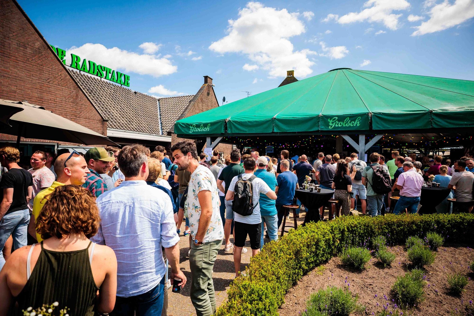 Gasten op een terras met een groene parasol en een kraan op de achtergrond tijdens een bedrijfsfeest, gemaakt door Bold Productions