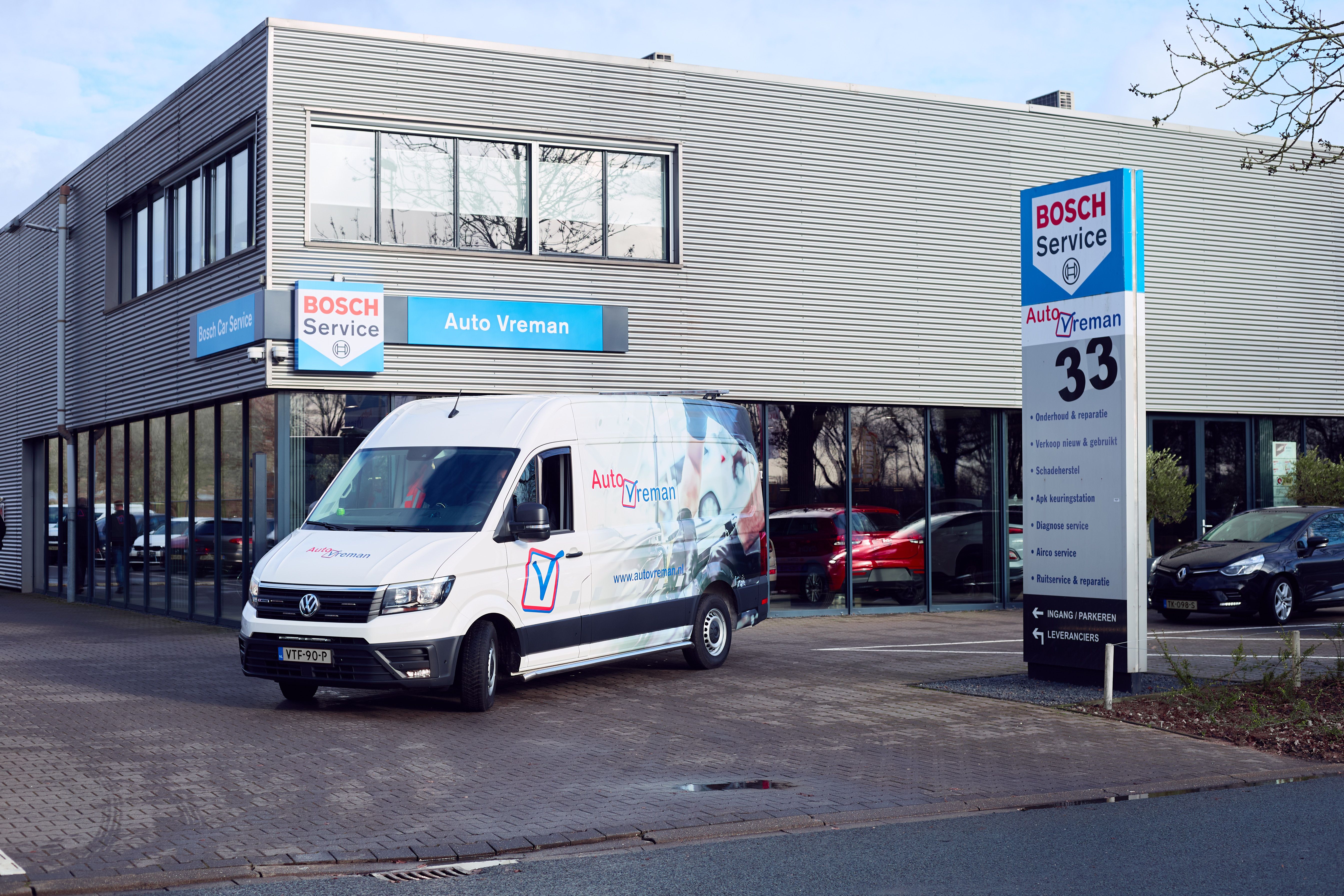 Bedrijfsbus met belettering staat voor het pand van Auto Vreman.