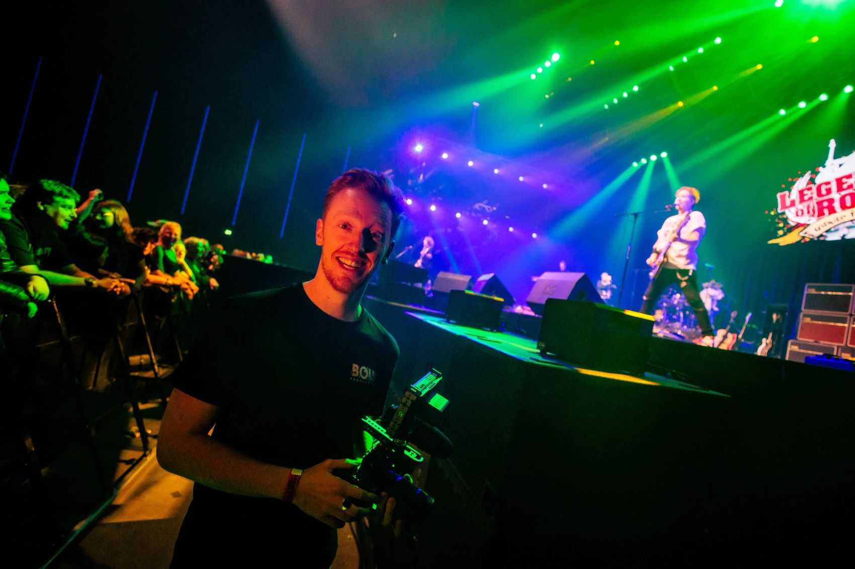 Cameraman van Bold Productions voor het podium tijdens een concert in groen licht.