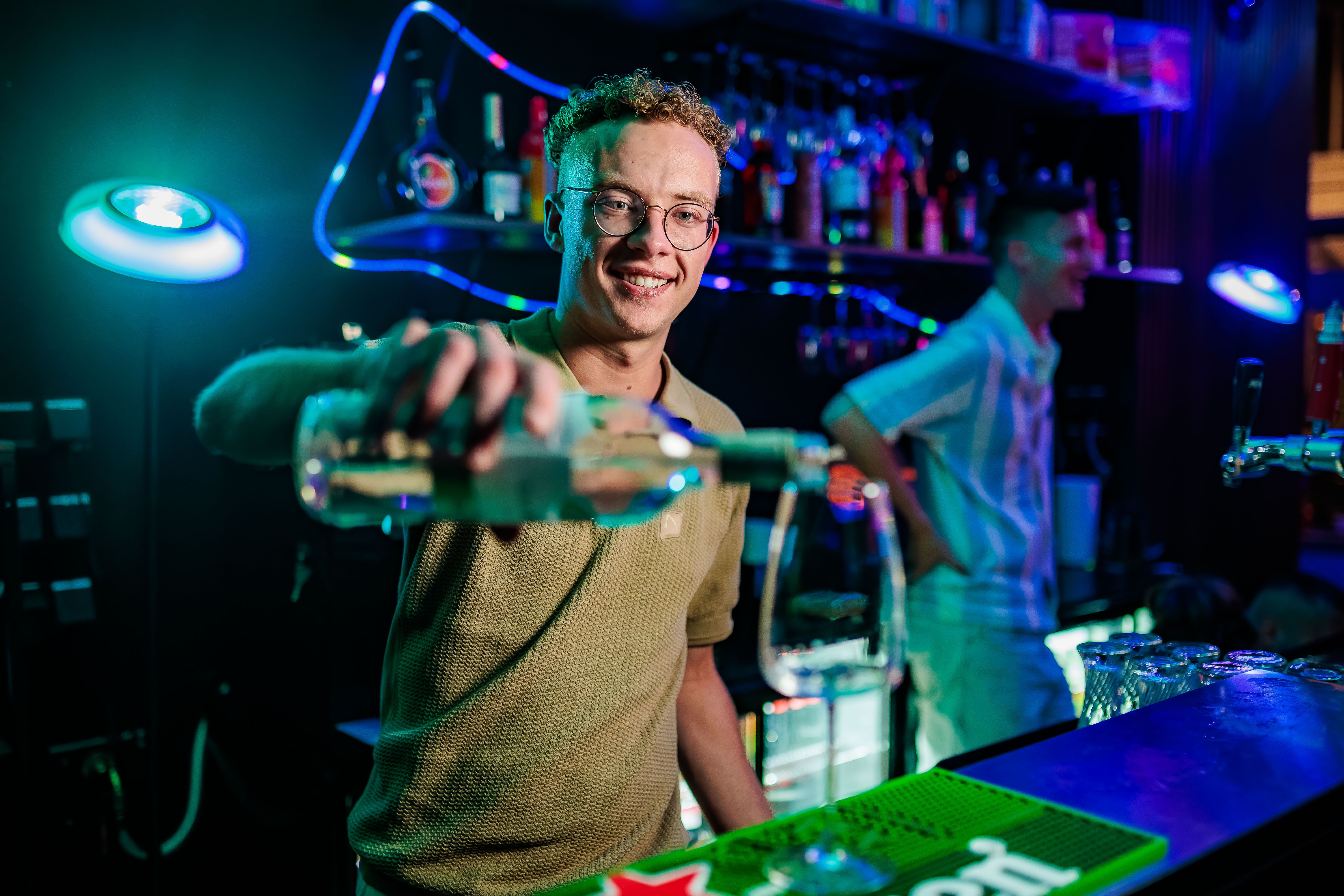 Barman met bril schenkt een shot in achter de bar met neonverlichting, gemaakt door Bold Productions