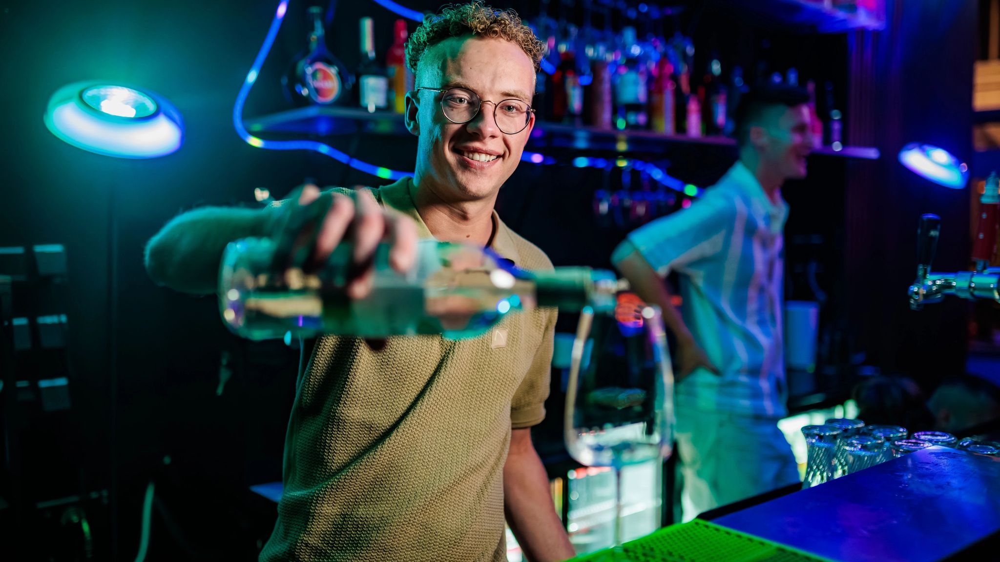 Barman met bril schenkt een shot in achter de bar met neonverlichting, gemaakt door Bold Productions