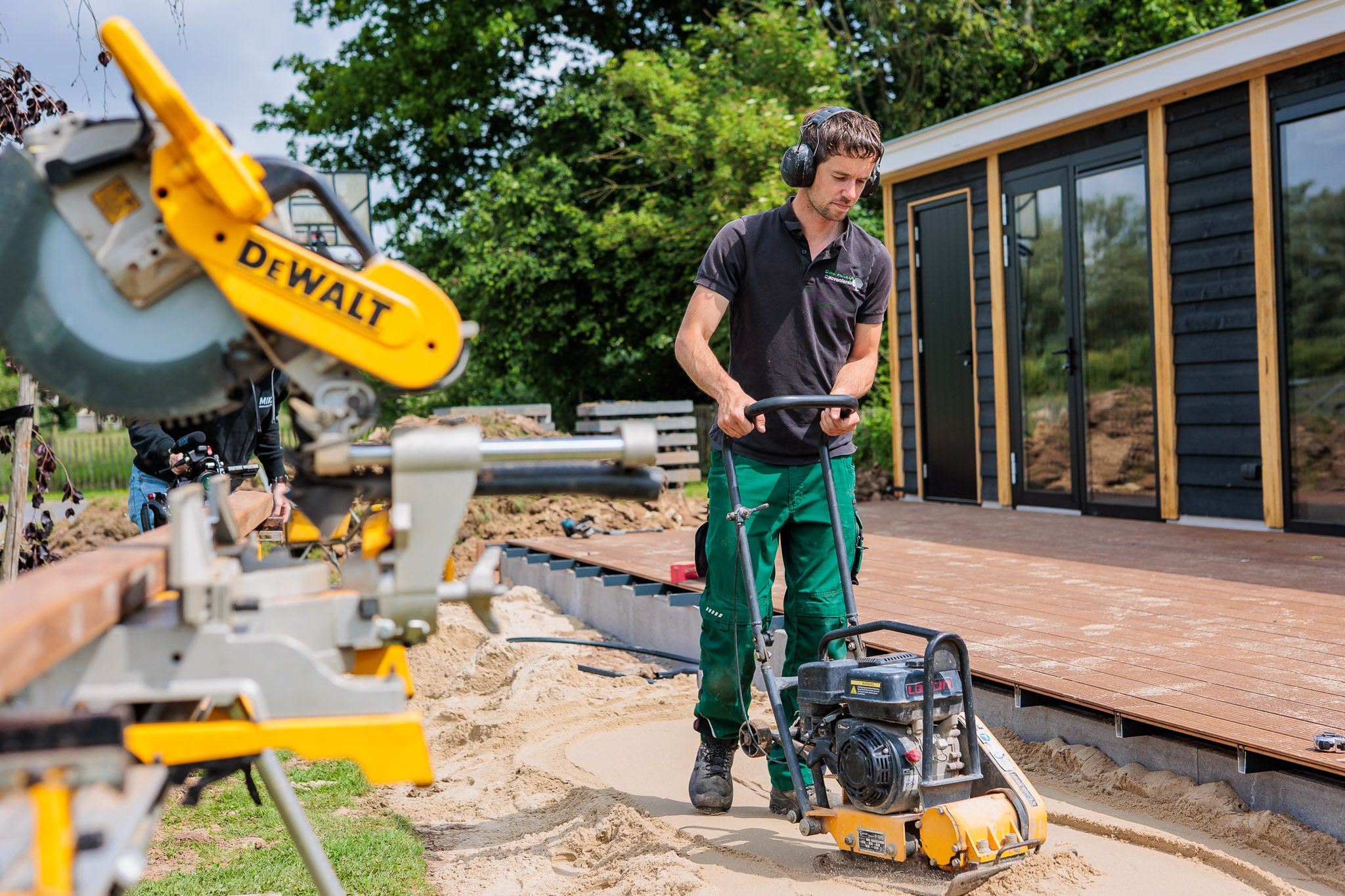 Hovenier werkt met een trilplaat naast een afkortzaag.