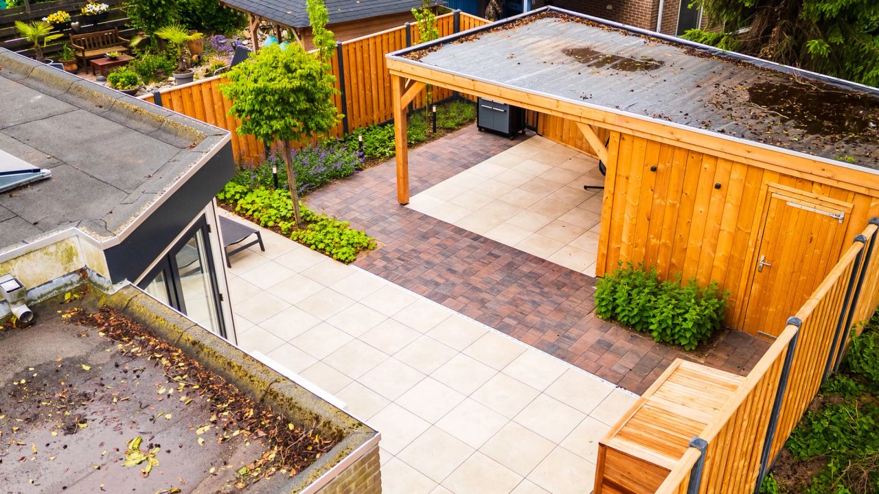 Luchtfoto van een terras met grote tegels en een houten overkapping in een tuin.