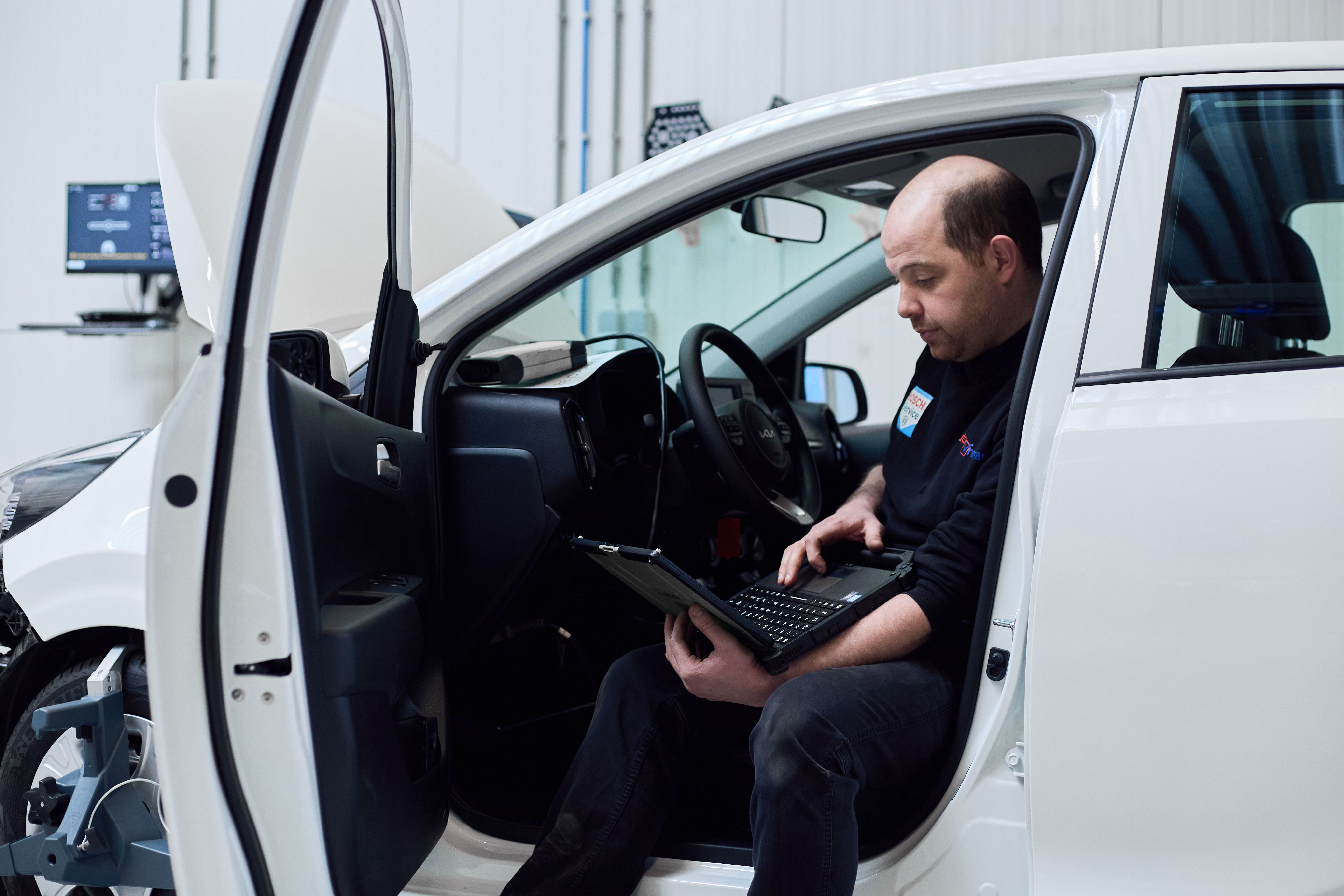 Monteur zit in een witte auto en leest het systeem uit met een laptop.