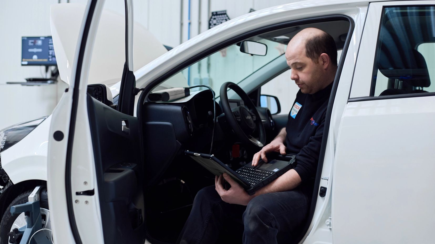 Monteur zit in een witte auto en leest het systeem uit met een laptop.