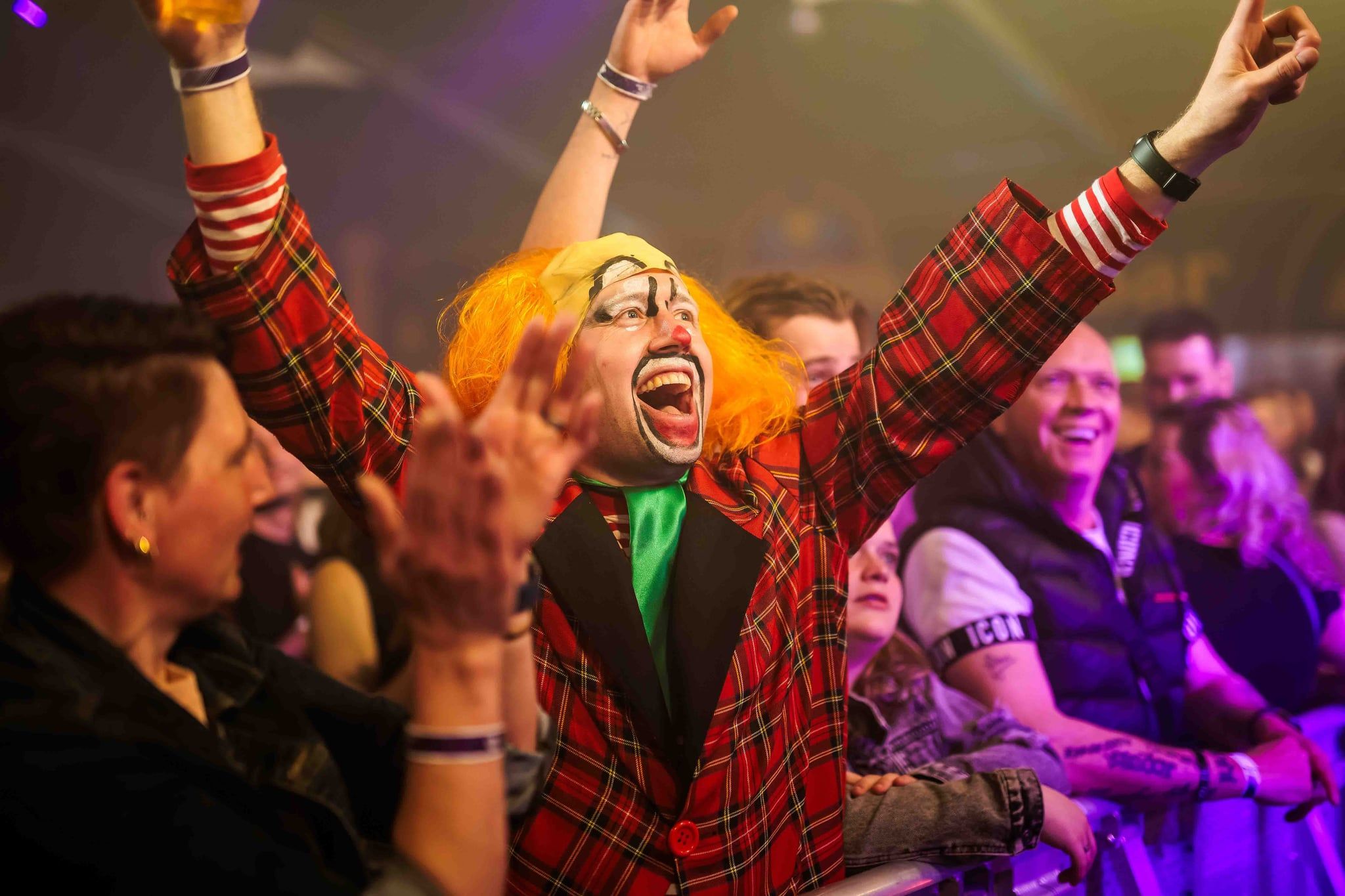 Feestganger in een rood geruit jasje en gekleurde pruik juicht met opgeheven armen tijdens het Doorgedraaid Feestival, gemaakt door Bold Productions