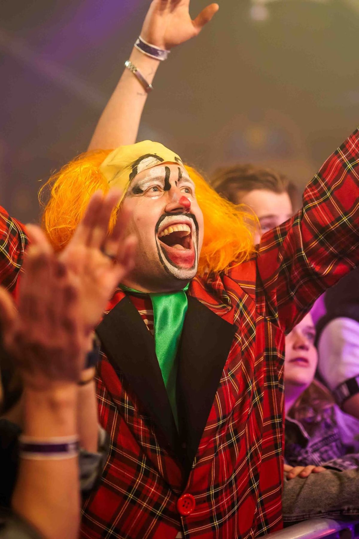 Feestganger in een rood geruit jasje en gekleurde pruik juicht met opgeheven armen tijdens het Doorgedraaid Feestival, gemaakt door Bold Productions