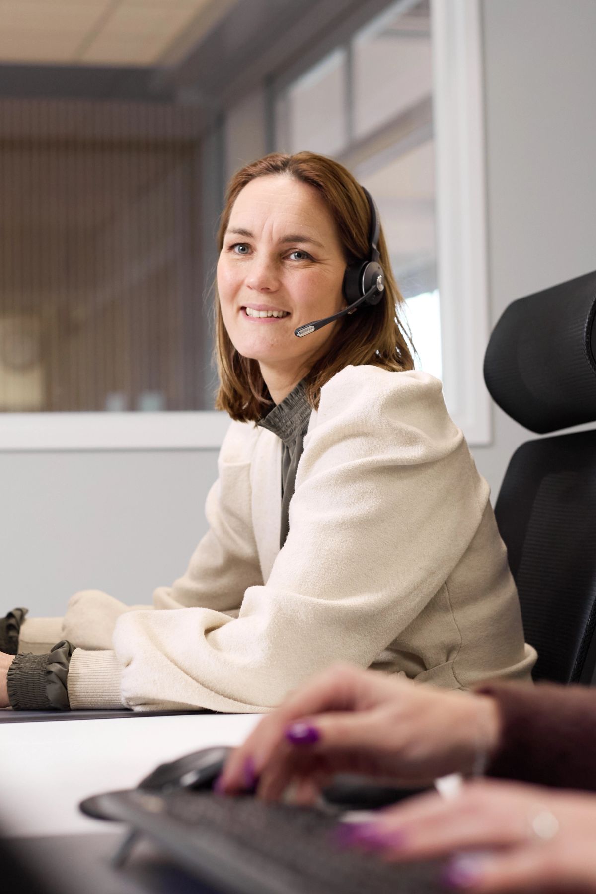 Lachende medewerkster met headset aan haar bureau op kantoor.