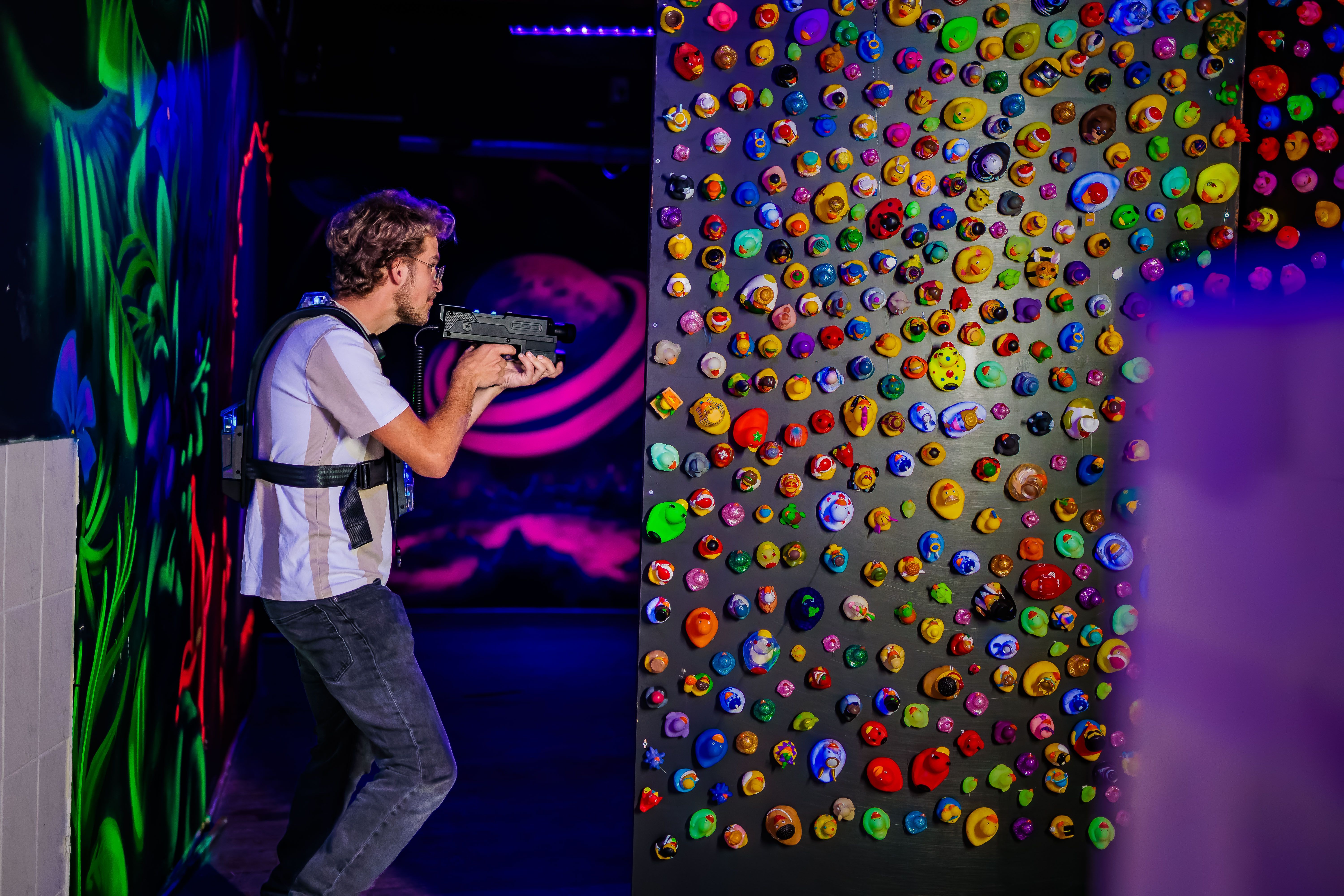 Lasergamer mikt in een donkere arena met een kleurrijke noppenwand.