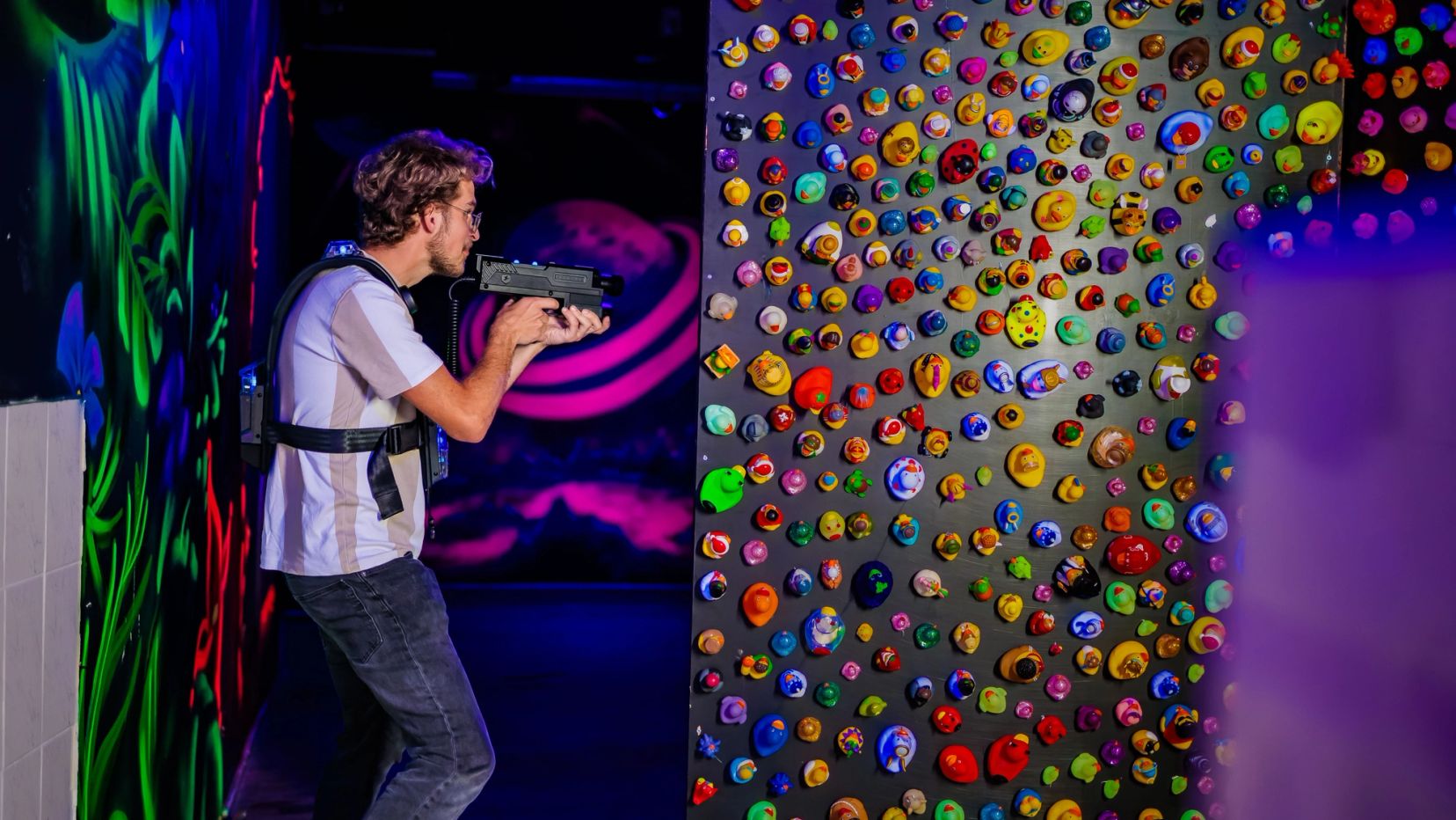 Lasergamer mikt in een donkere arena met een kleurrijke noppenwand.