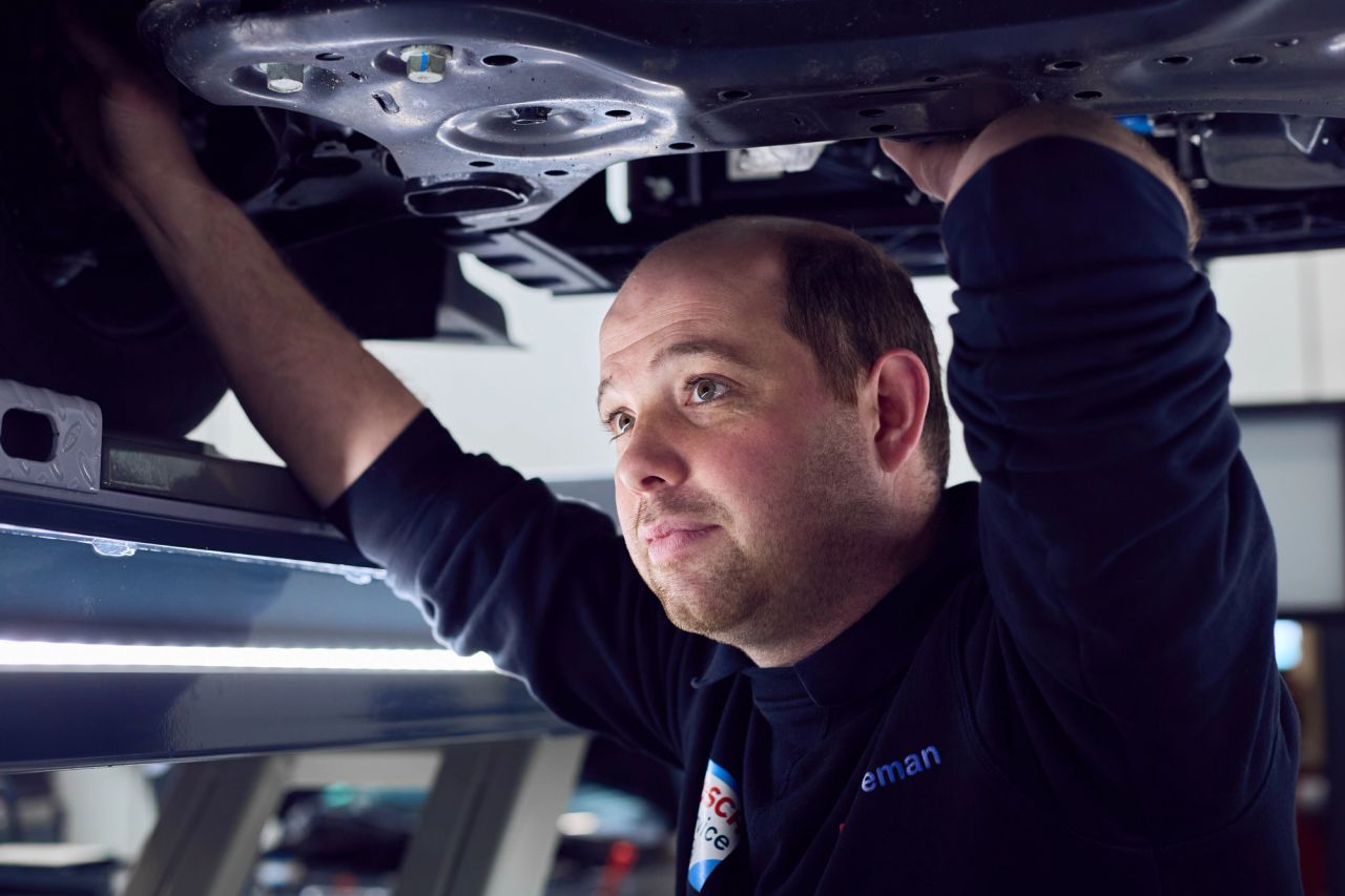 Monteur werkt aan het onderstel van een auto op de brug.