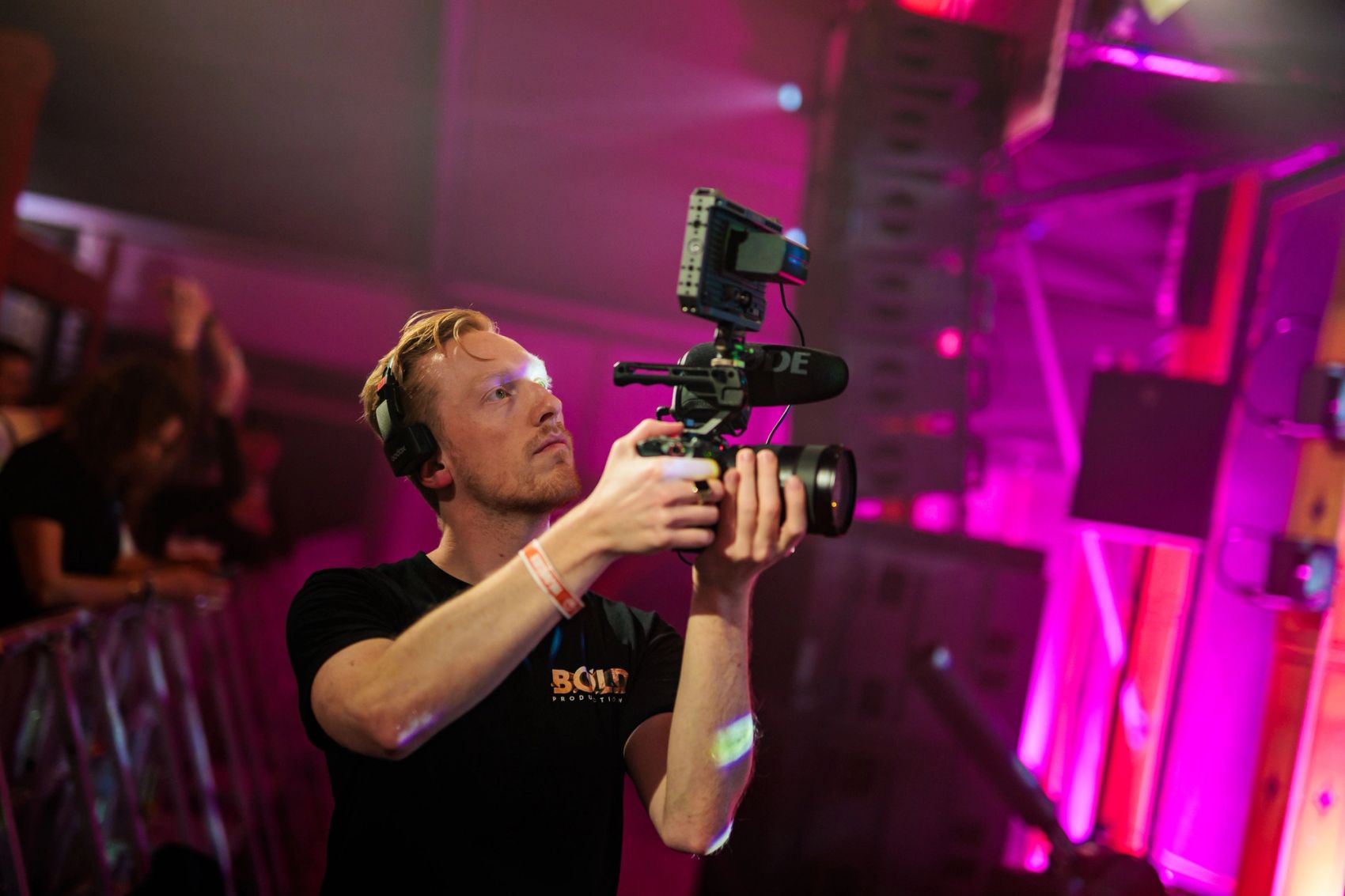 Cameraman van Bold Productions filmt backstage in roze licht.