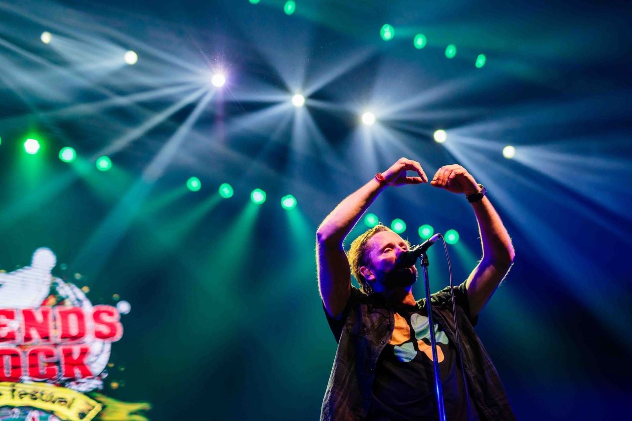 Zanger maakt een hart met zijn handen op het podium van Legends of Rock in blauwe lichtbundels, gemaakt door Bold Productions