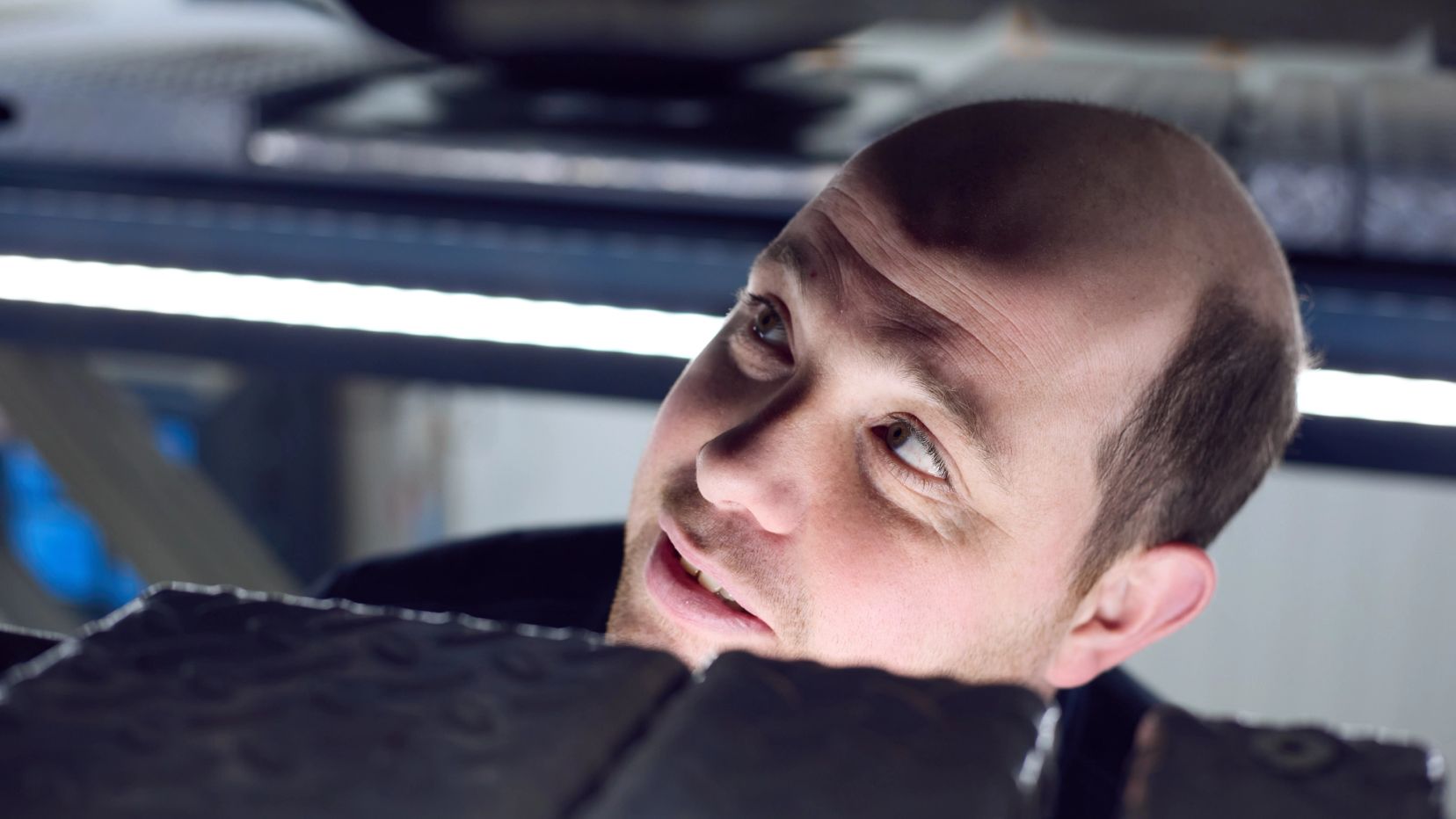 Monteur kijkt omhoog naar het onderstel van een auto in de werkplaats.