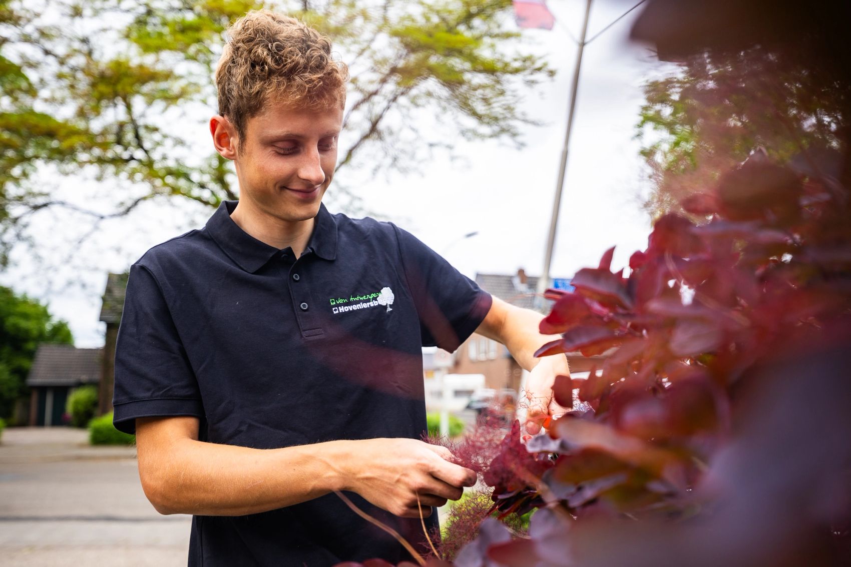 Portret van een jonge hovenier met een snoeischaar bij een struik met rode bladeren, gemaakt door Bold Productions