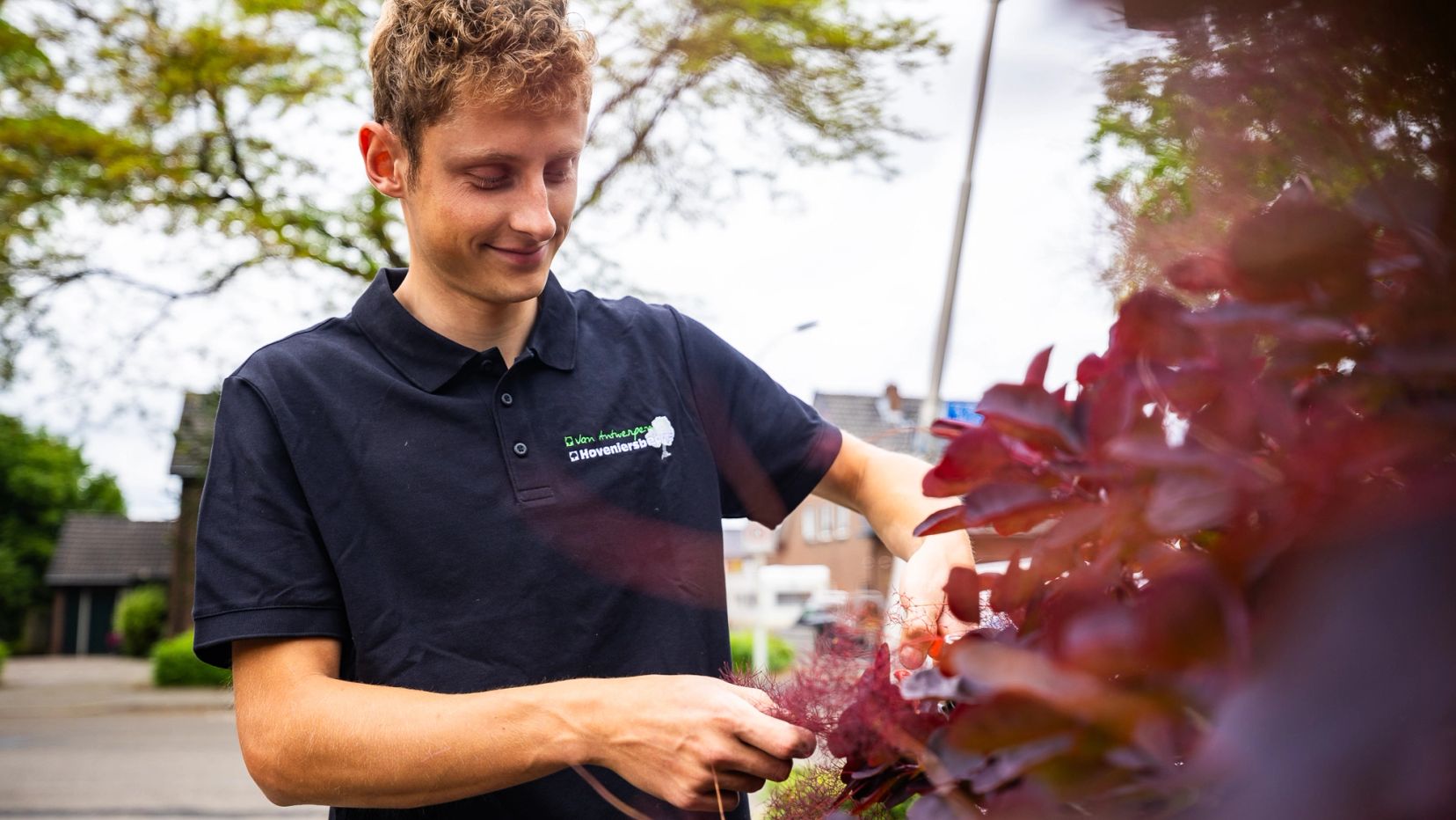 Portret van een jonge hovenier met een snoeischaar bij een struik met rode bladeren.