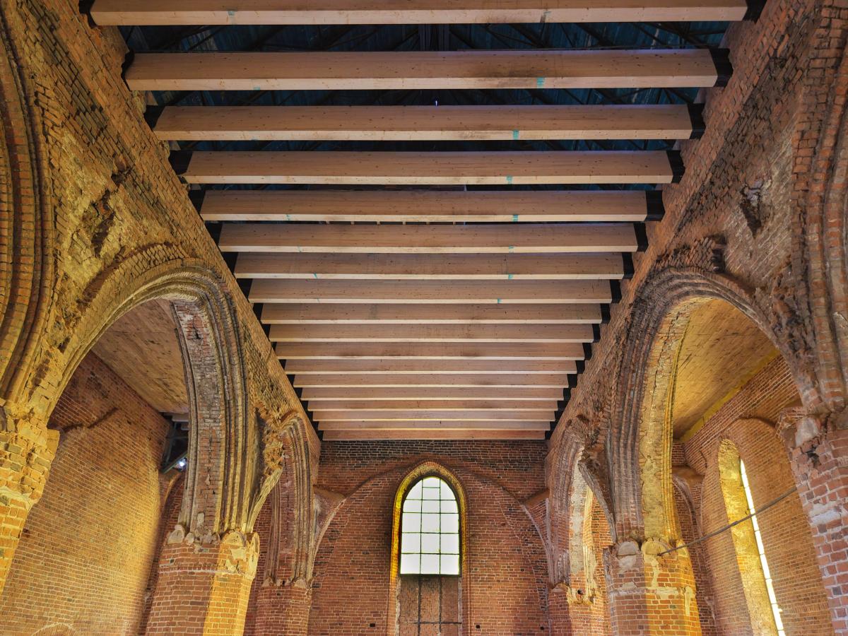 Wnętrze zabytkowego budynku z widoczną nową konstrukcją stropu drewnianego, ukazujące etap rewaloryzacji i adaptacji architektury historycznej do współczesnych potrzeb.