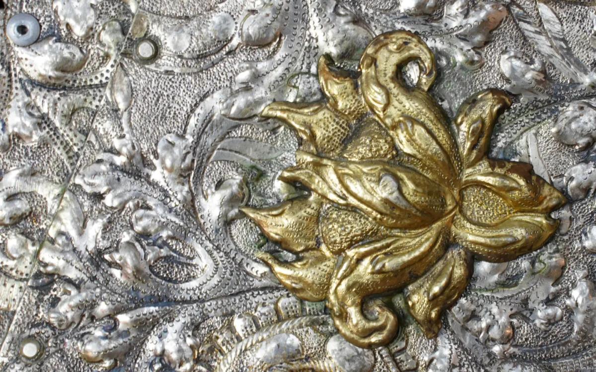 Zbliżenie na zdobiony ornament metalowy z pozłacanym motywem roślinnym w stylu barokowym, przedstawiające detale pracy konserwatorskiej przy rzemiośle artystycznym.