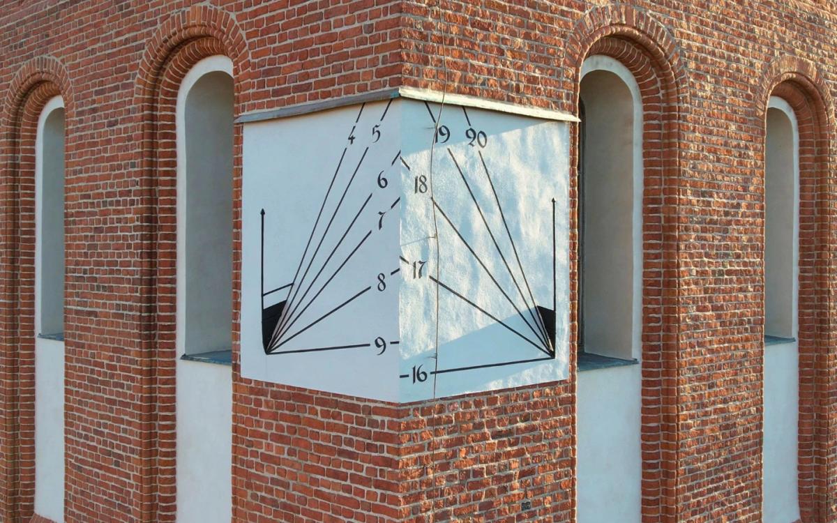 Odrestaurowany zegar słoneczny na narożniku elewacji Wieży Radziejowskiego we Fromborku, z precyzyjnie odtworzonymi liniami godzinowymi na tle ceglanej architektury.