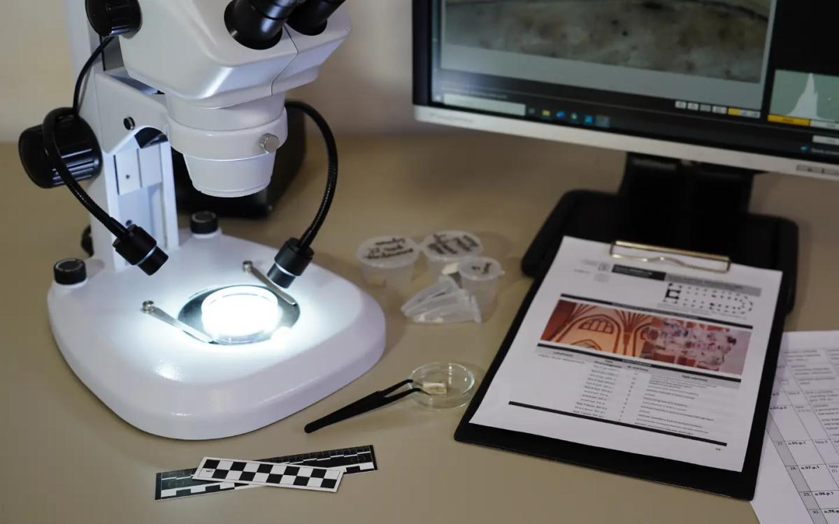 Stanowisko laboratoryjne w RenomaLAB z mikroskopem, próbkami materiałów, dokumentacją stratygraficzną i ekranem z obrazem mikroskopowym, wykorzystywane do badań konserwatorskich.