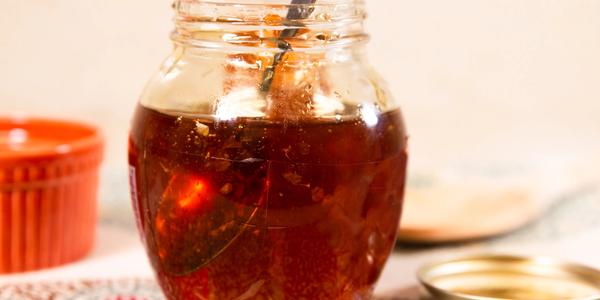 A small glass jar of pale honey beside a piece of honeycomb