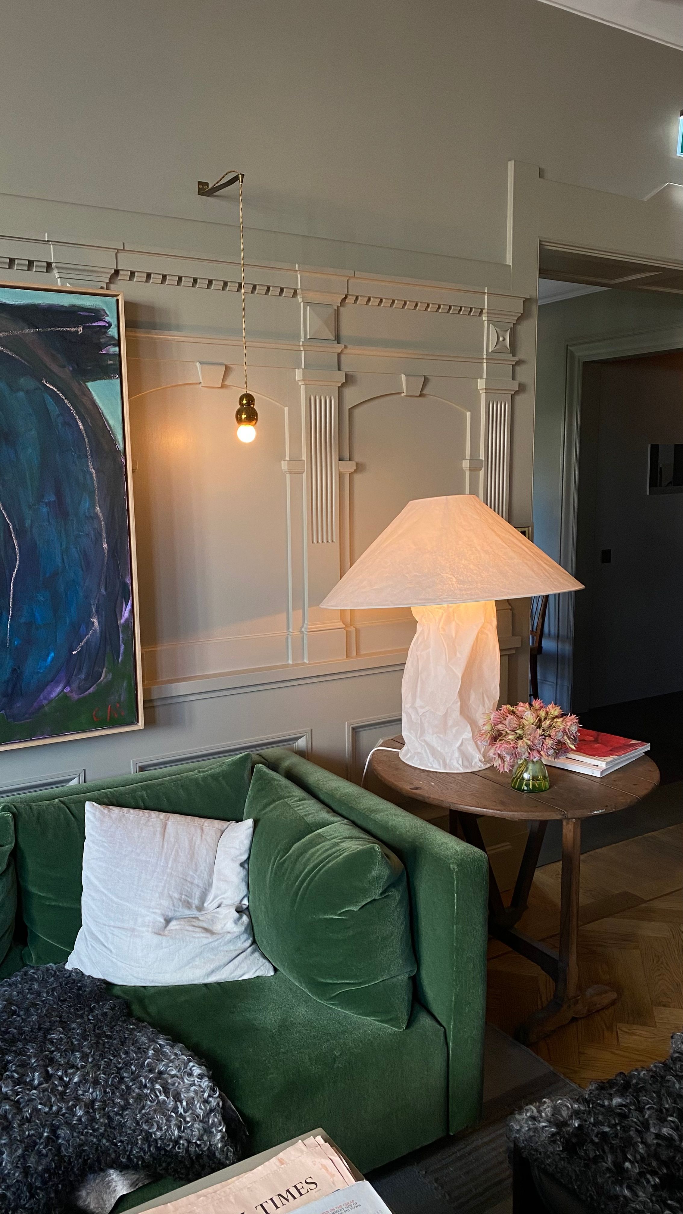 A lived-in room with green seating, books, art and warm lamplight