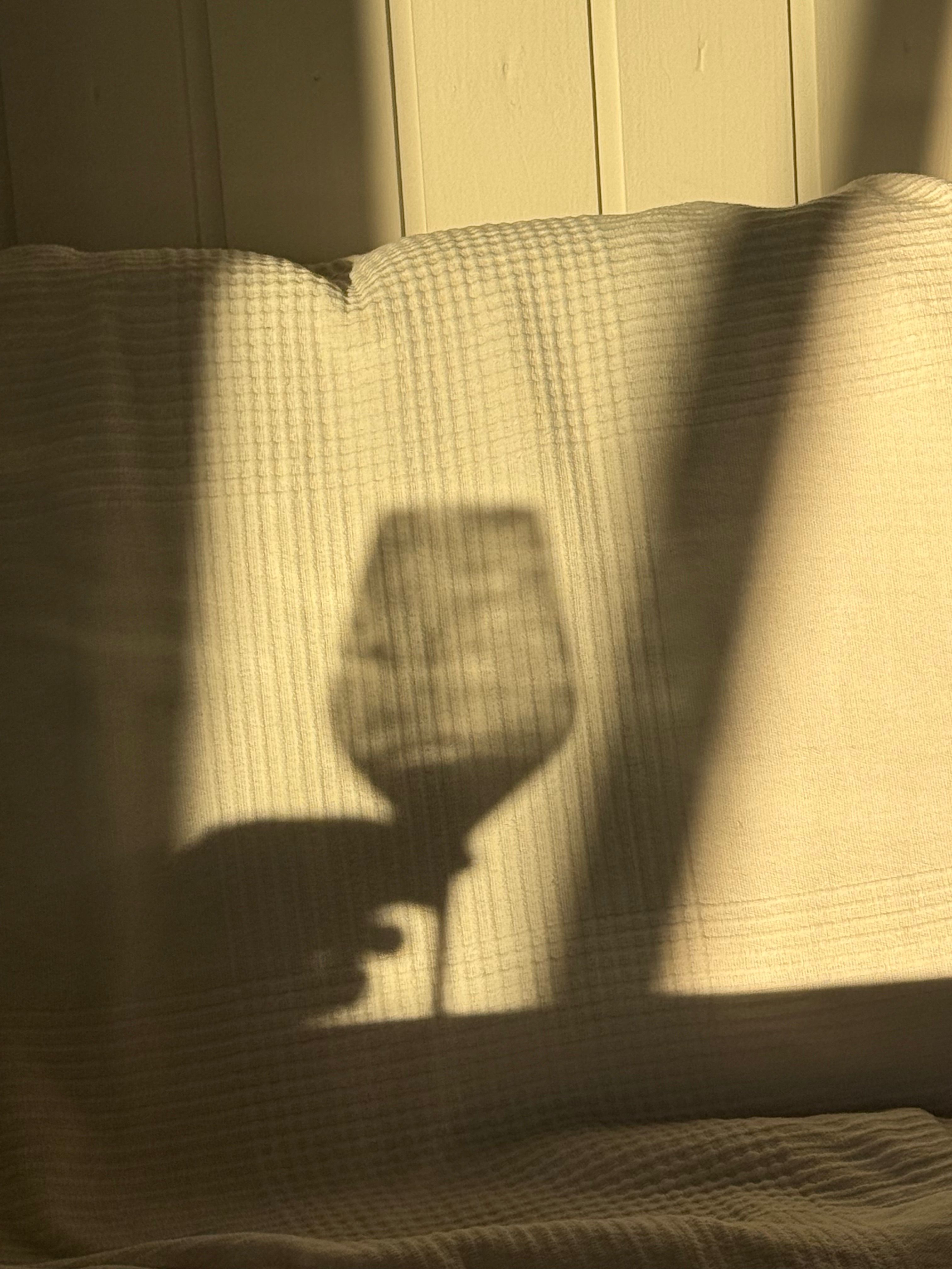 Der Schatten eines Weinglases auf einem Stuhl im Sonnenlicht