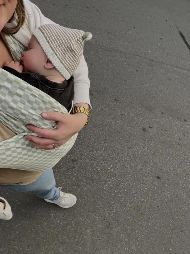 Ein Baby schläft in einer karierten Trage