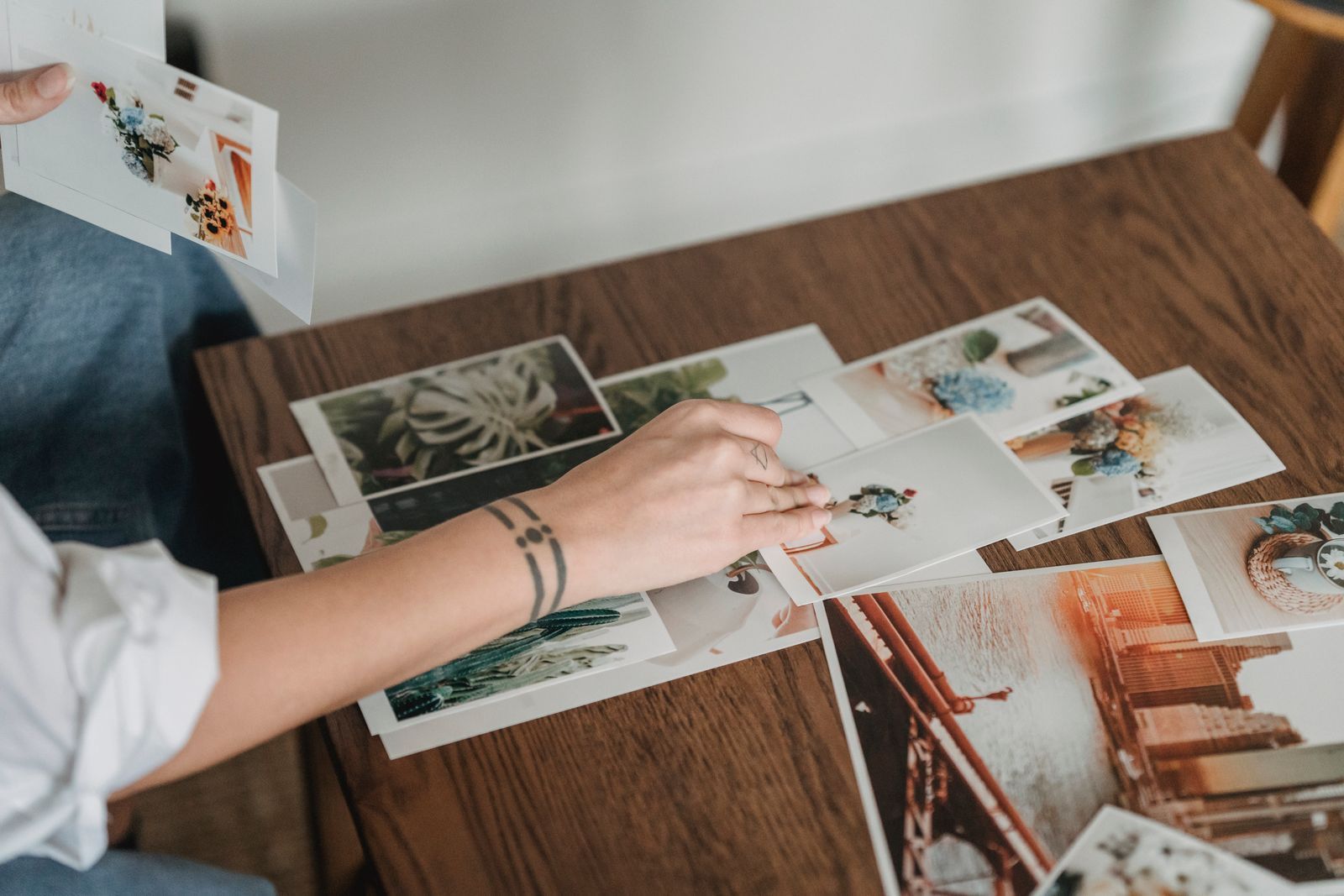 Hands selecting and arranging personal photographs on a wooden table