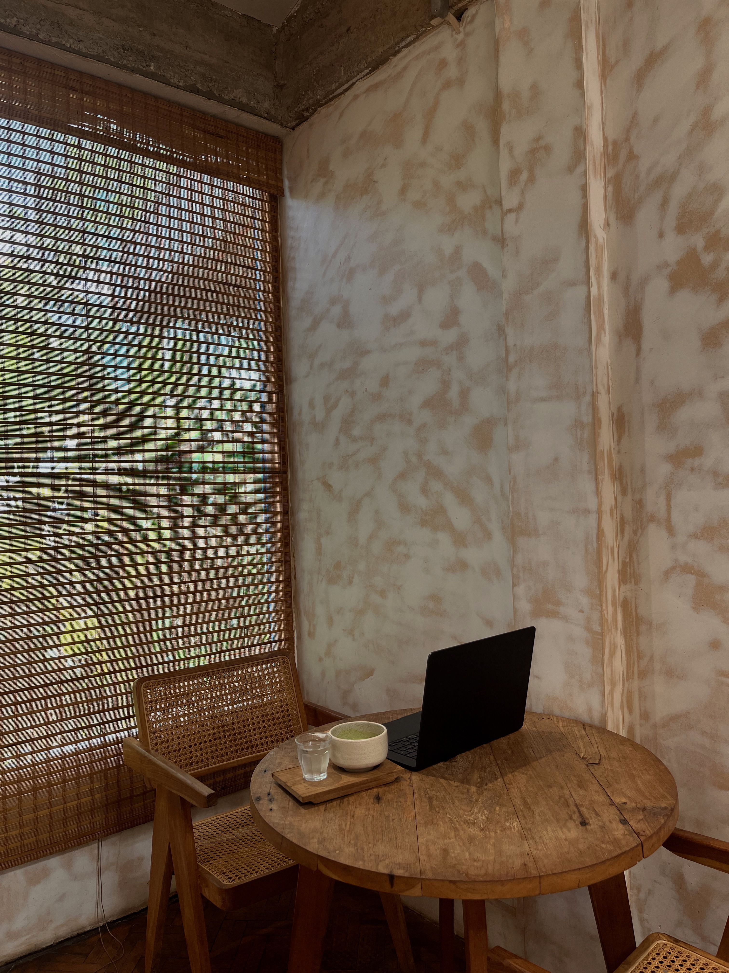 Ein Laptop und eine Tasse Matcha auf einem Holztisch am Caféfenster