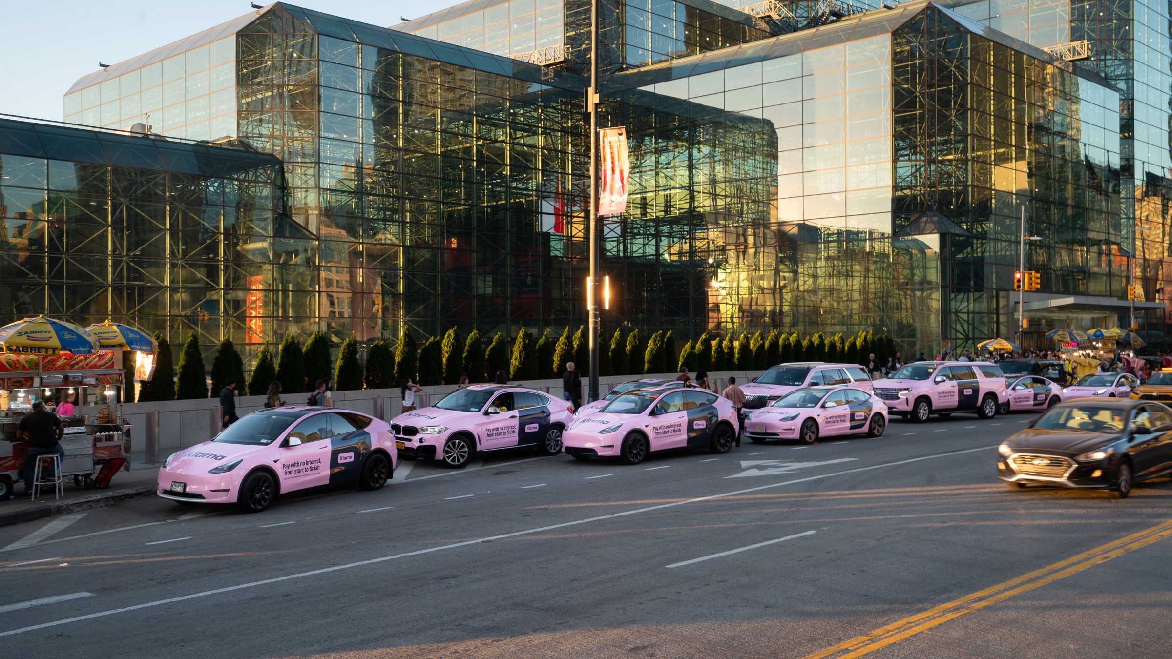Klarna-branded pink vehicle fleet parked outside the Jacob Javits Convention Center in New York City at dusk