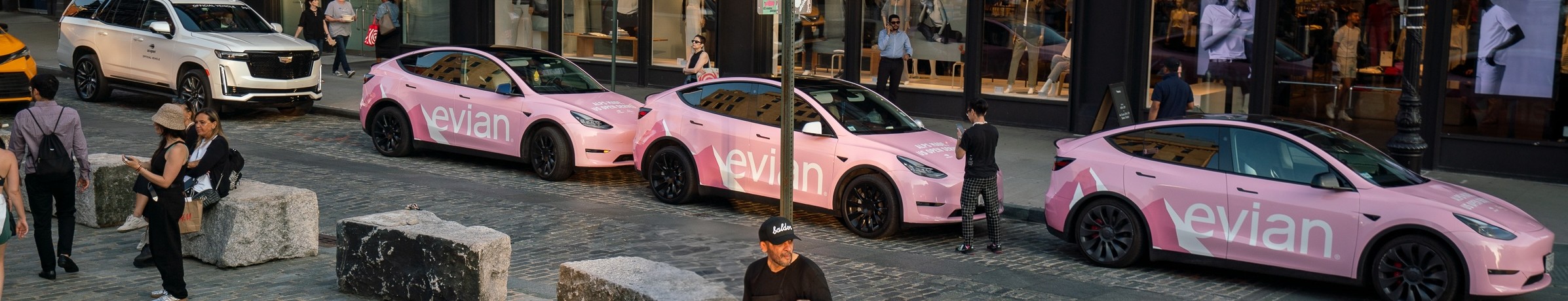 A fleet of rideshare vehicles wrapped with an advertisement for Evian parked on a city street