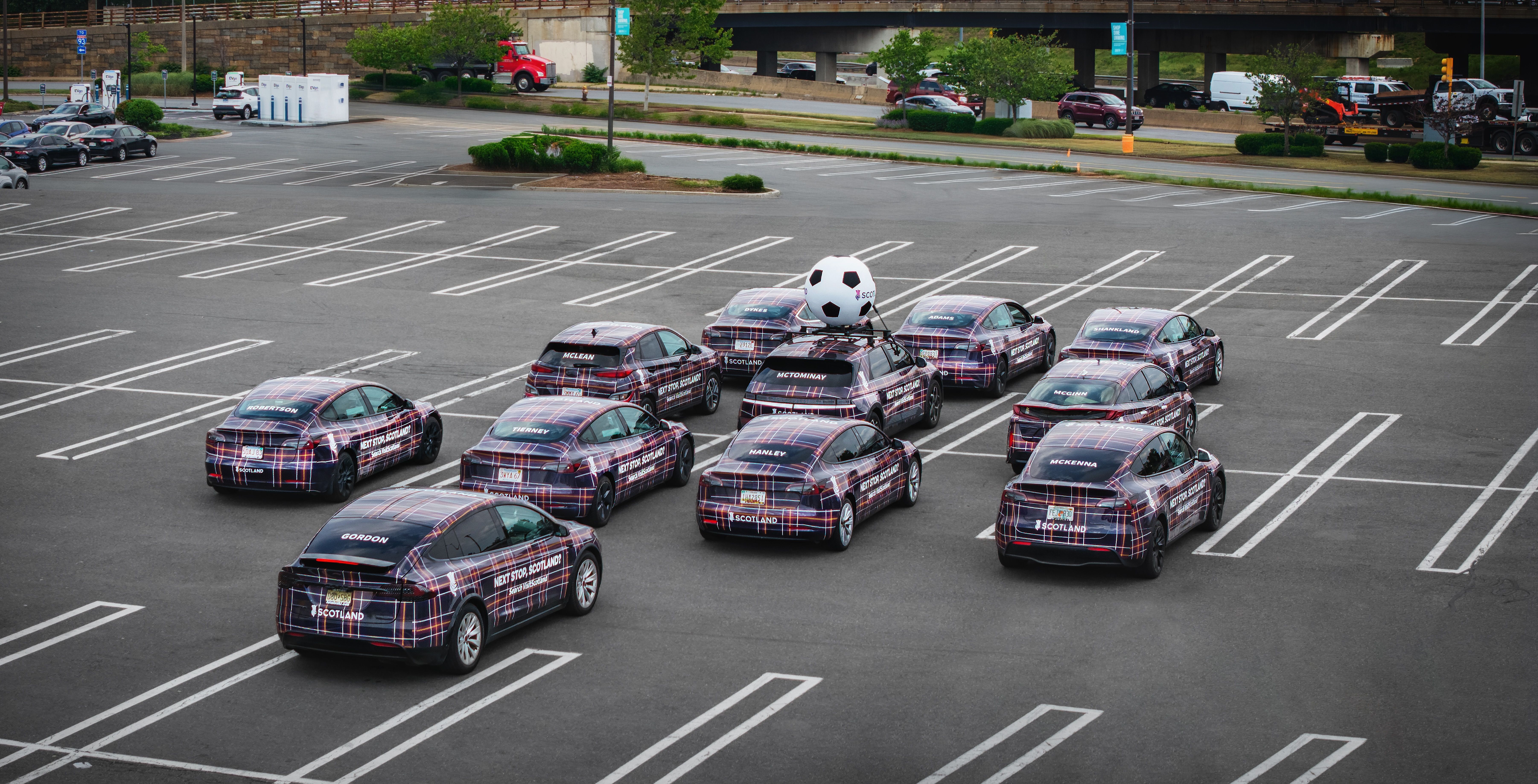 Wrapped cars in tartan for VisitScotland during 2026 FIFA World Cup in Boston; cars are positioned in parking lot to mirror the lineup of the Scottish football team